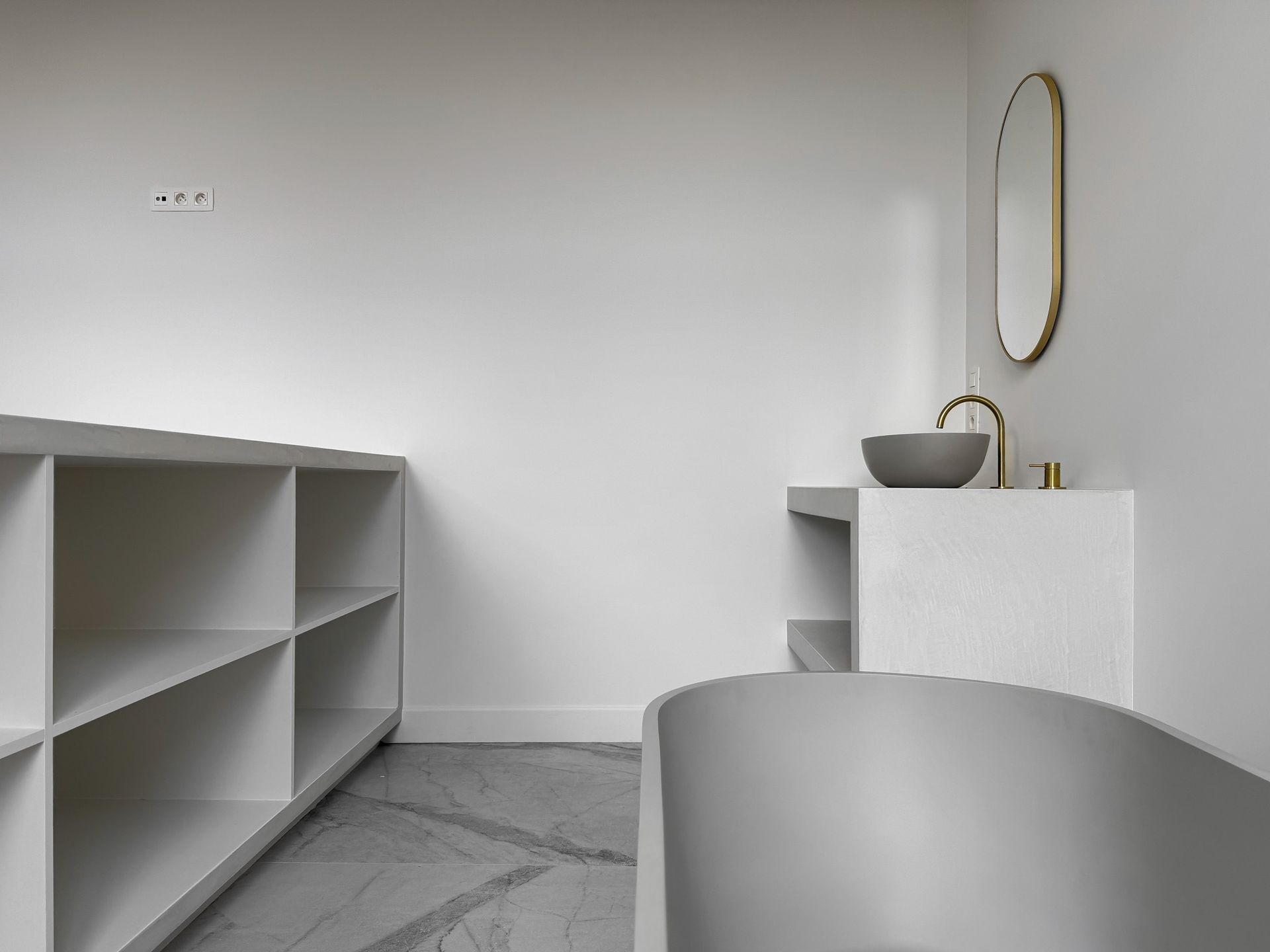 Moderne badkamer met een grijze wastafel, gouden kraan en witte kasten.