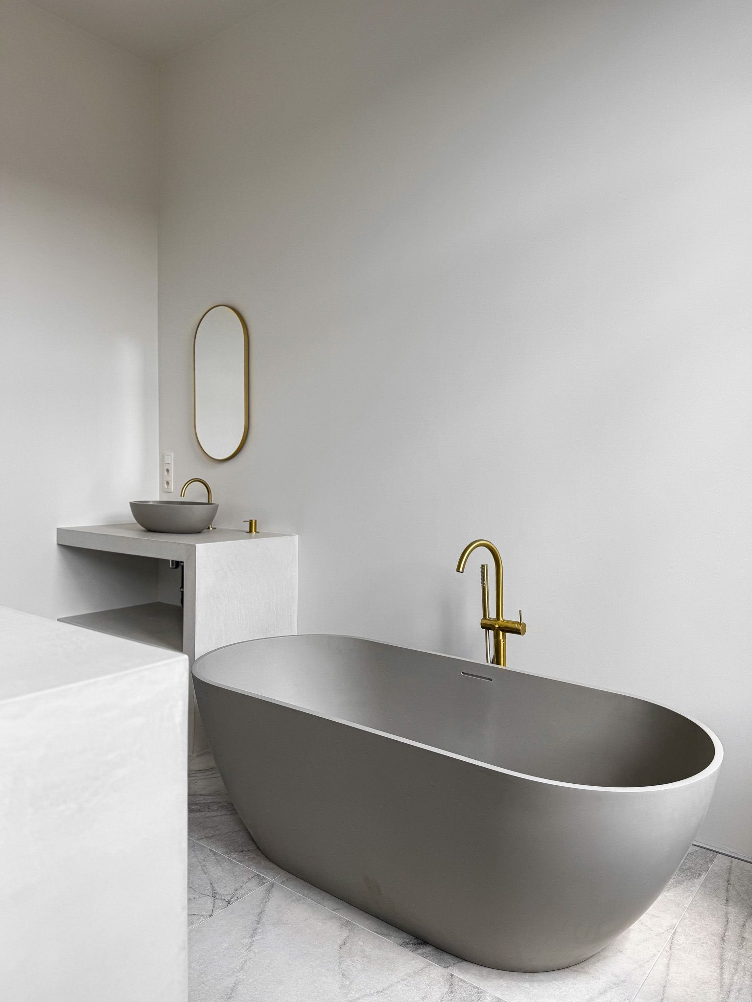 Moderne, grijze badkamer met ovaal bad, wastafel en gouden details.