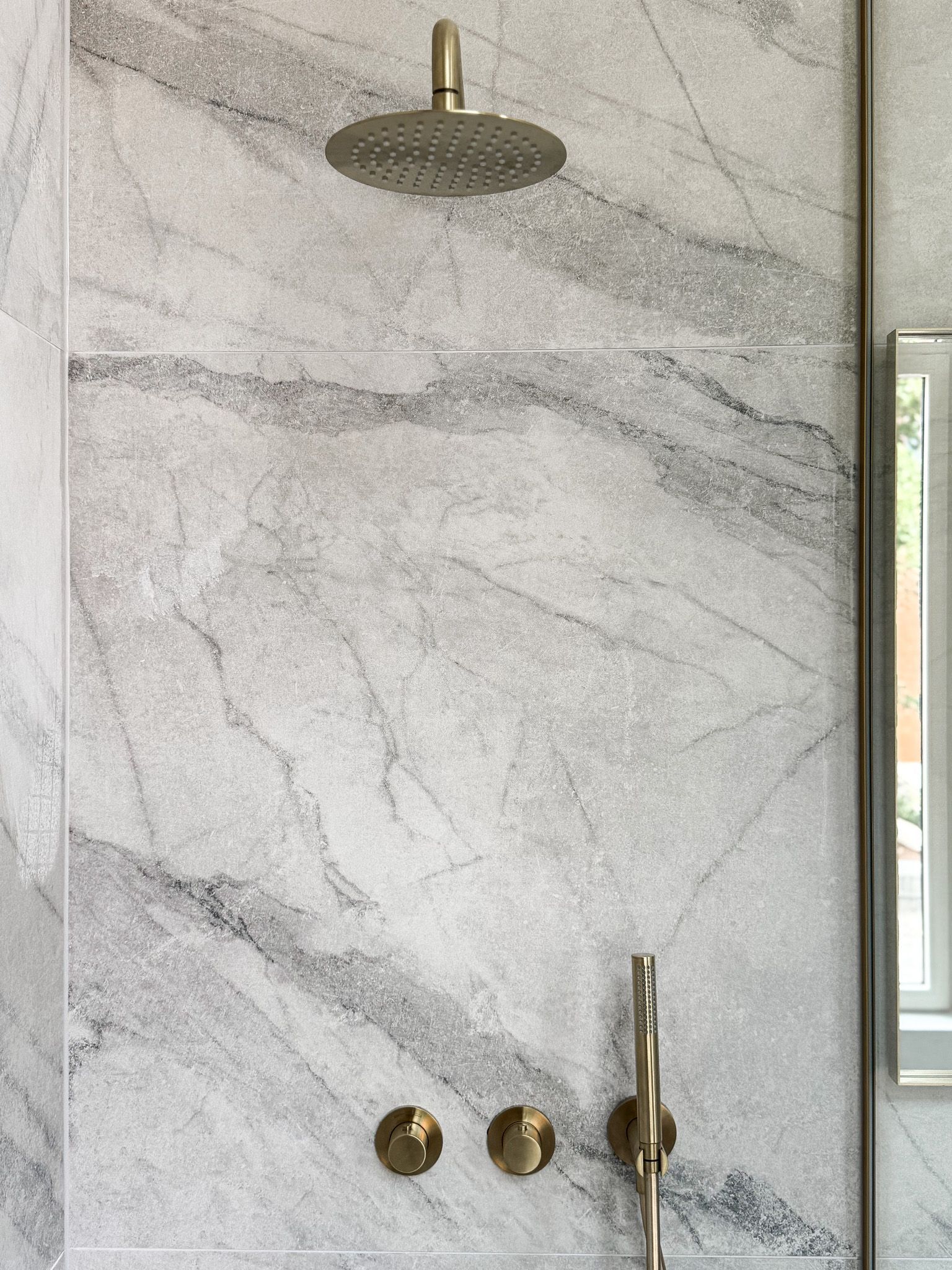 Douche met gouden armaturen tegen een muur van wit en grijs marmer.