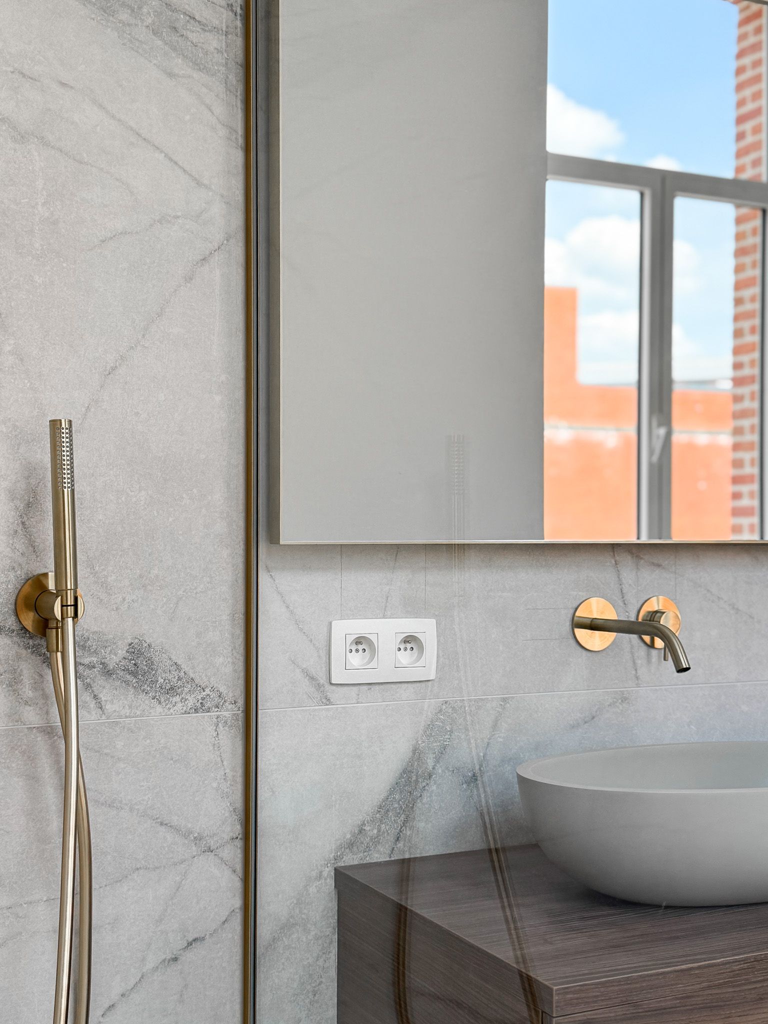 Moderne badkamer met marmeren muren, gouden details en een ronde wastafel.