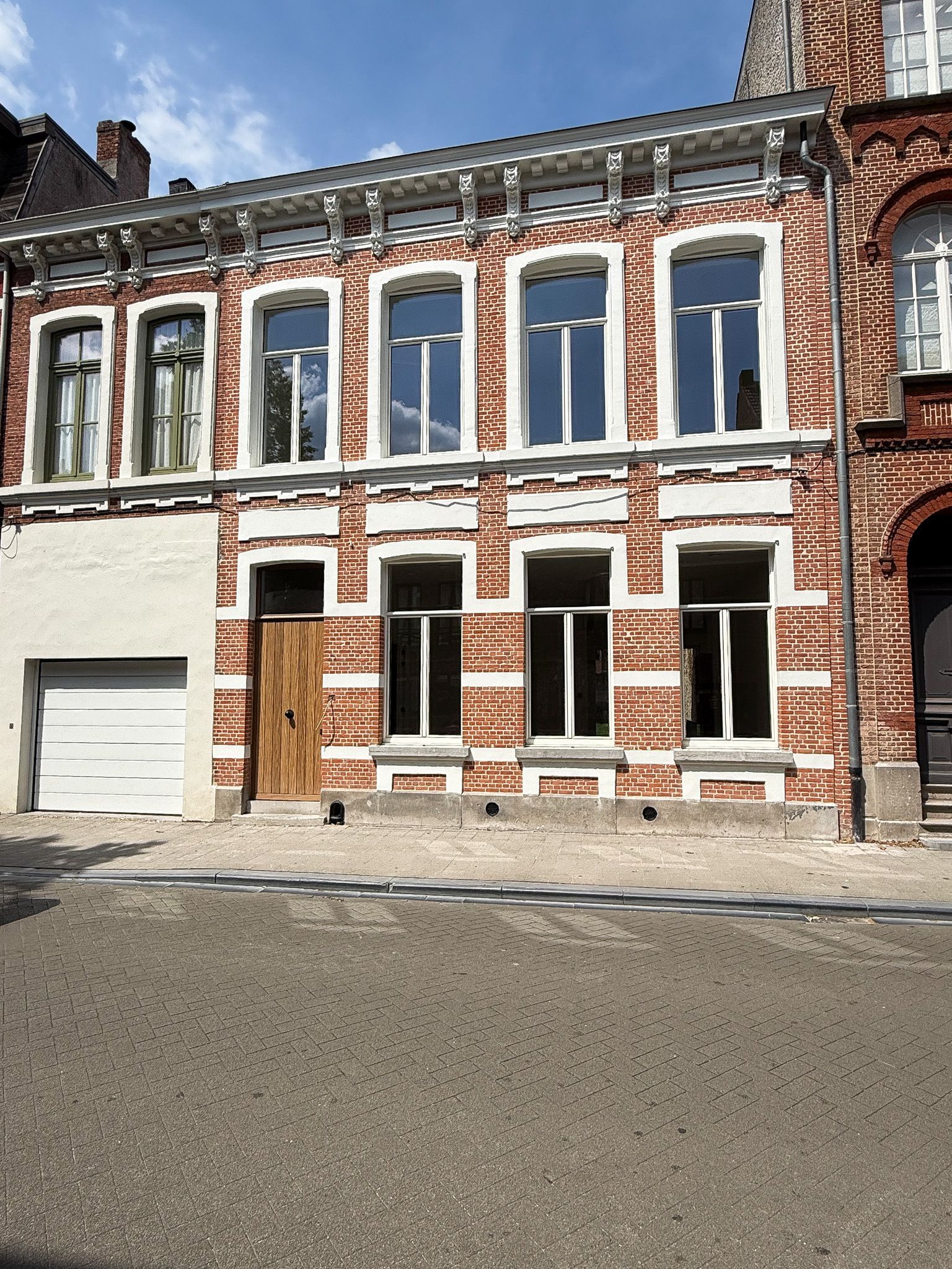 Bakstenen huis met witte lambrisering en grote ramen aan een geplaveide straat.