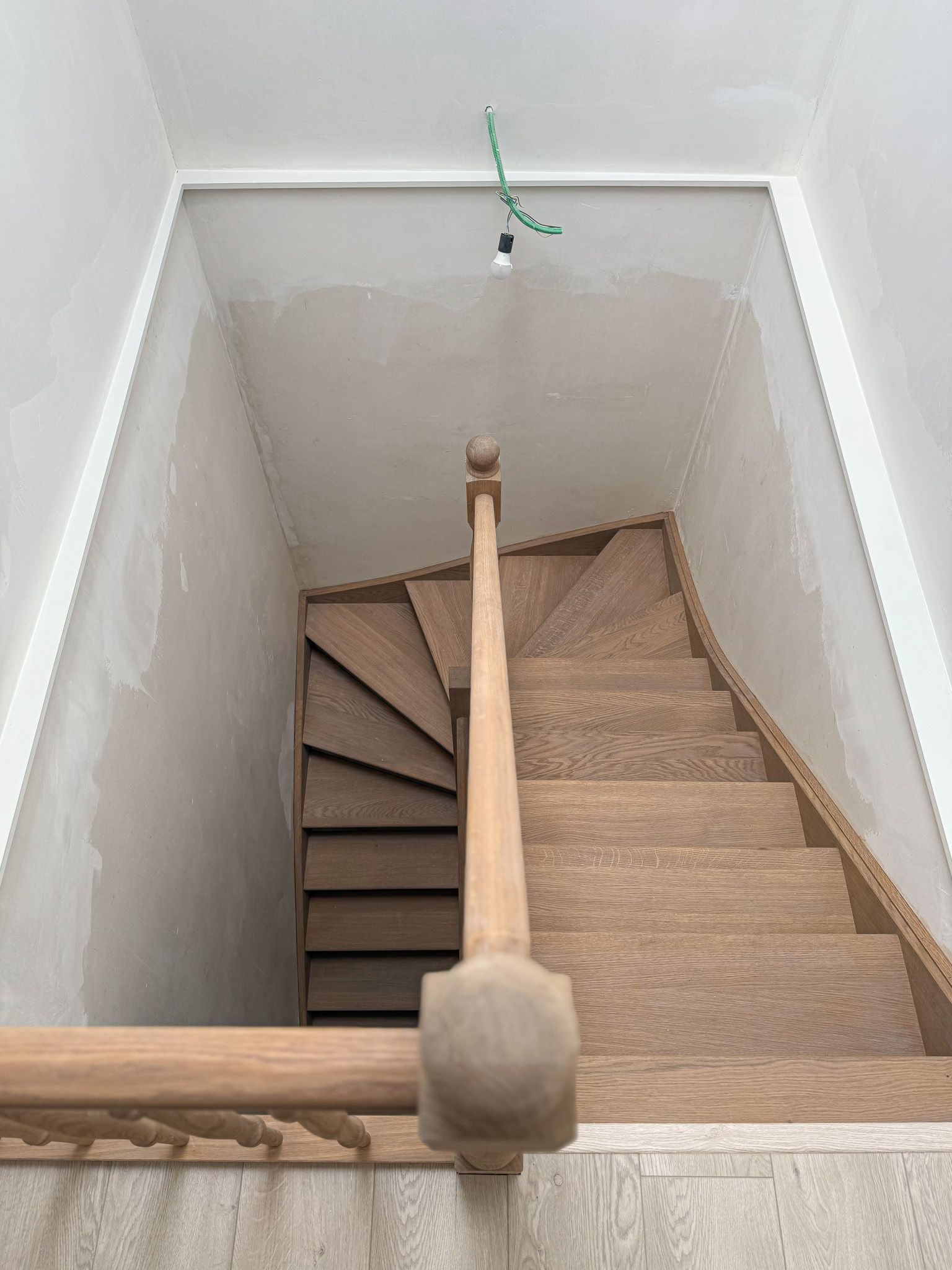 Een houten trap naar boven, met een lamp erboven, en witte muren.