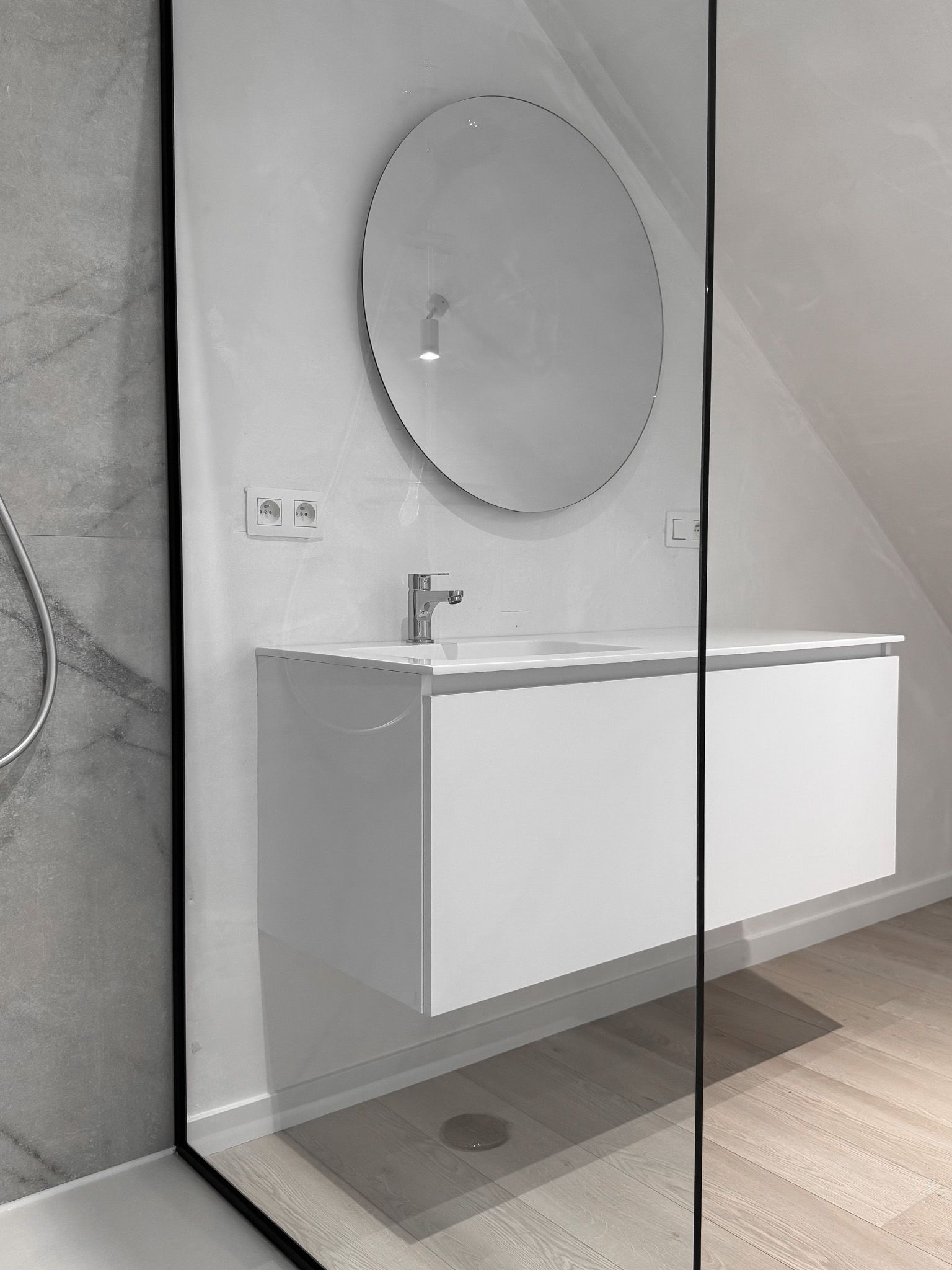Moderne badkamer met witte zwevende wastafel, ronde spiegel en douchecabine.