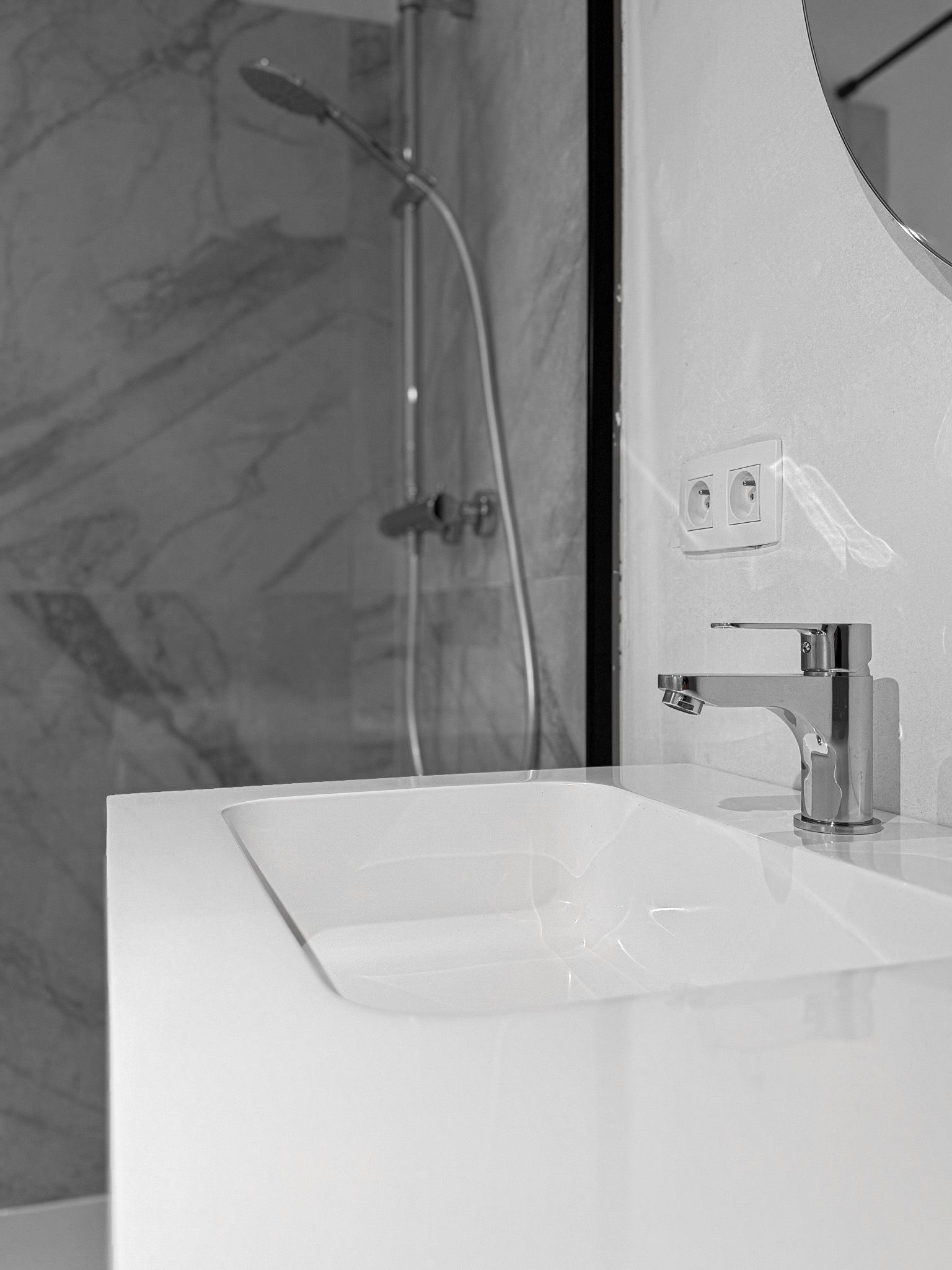Badkamerwastafel met chromen kraan en douche op de achtergrond, grijstinten.