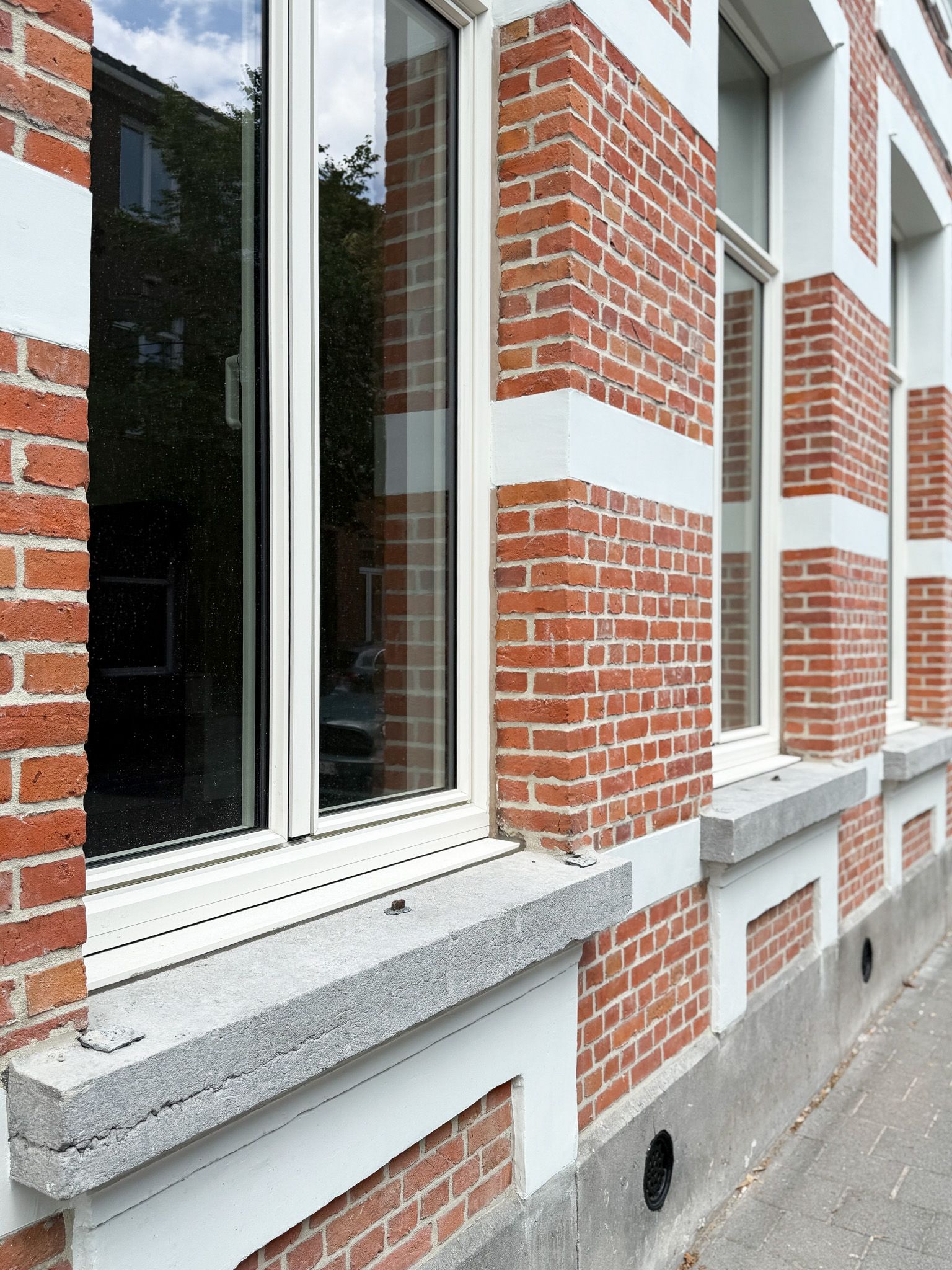 Gebouw van rode baksteen met witte kozijnen, granieten vensterbanken en een zichtbare weerspiegeling.