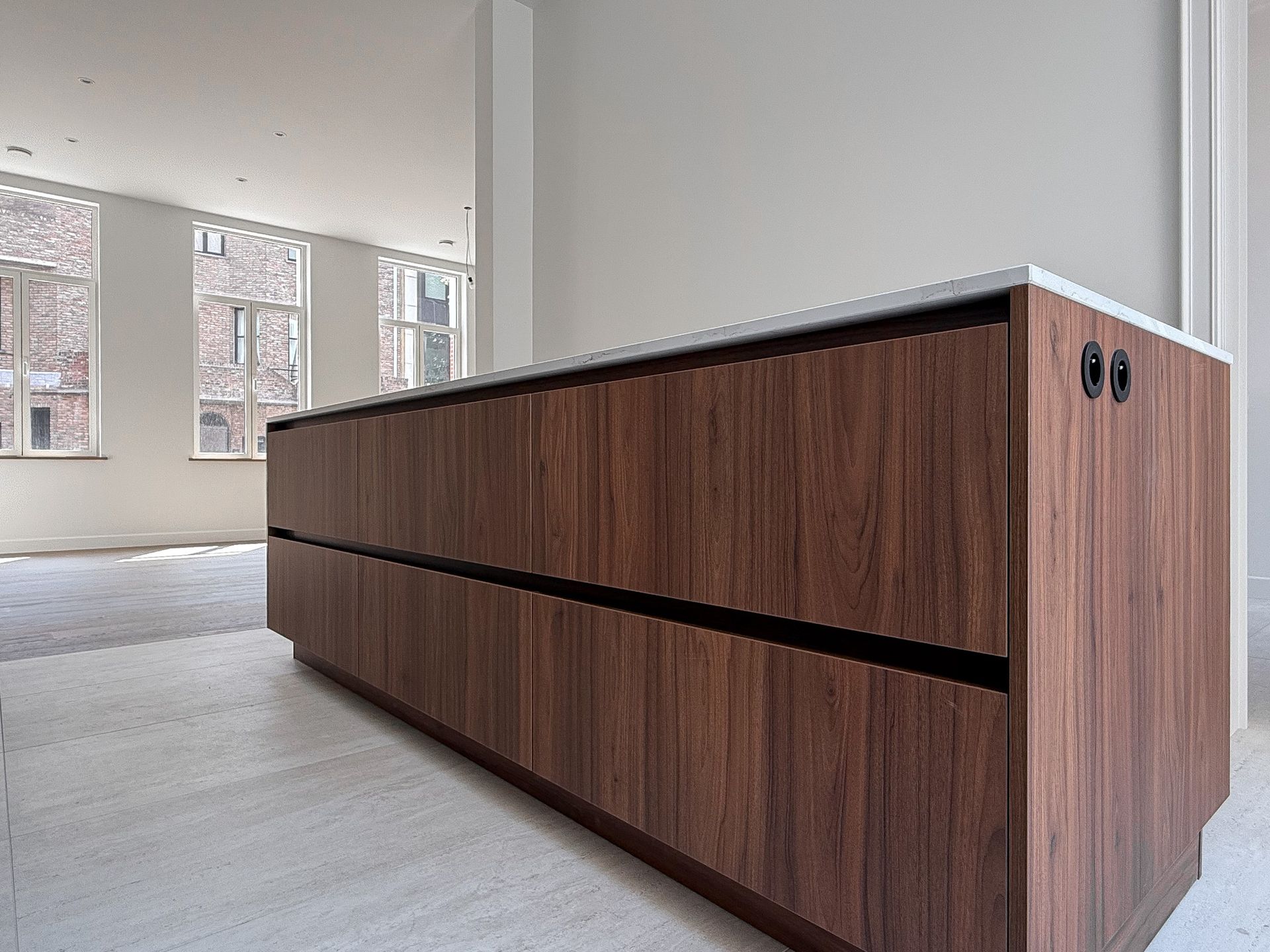 Houten kookeiland met licht aanrechtblad in een lichte kamer met ramen.