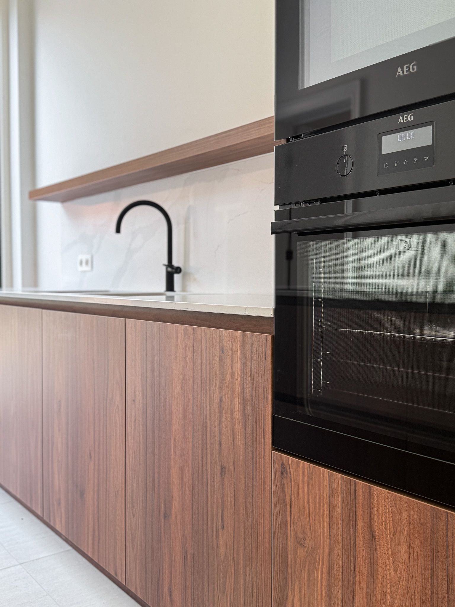 Moderne keuken met houten kasten, zwarte kraan en oven; een licht, minimalistisch ontwerp.