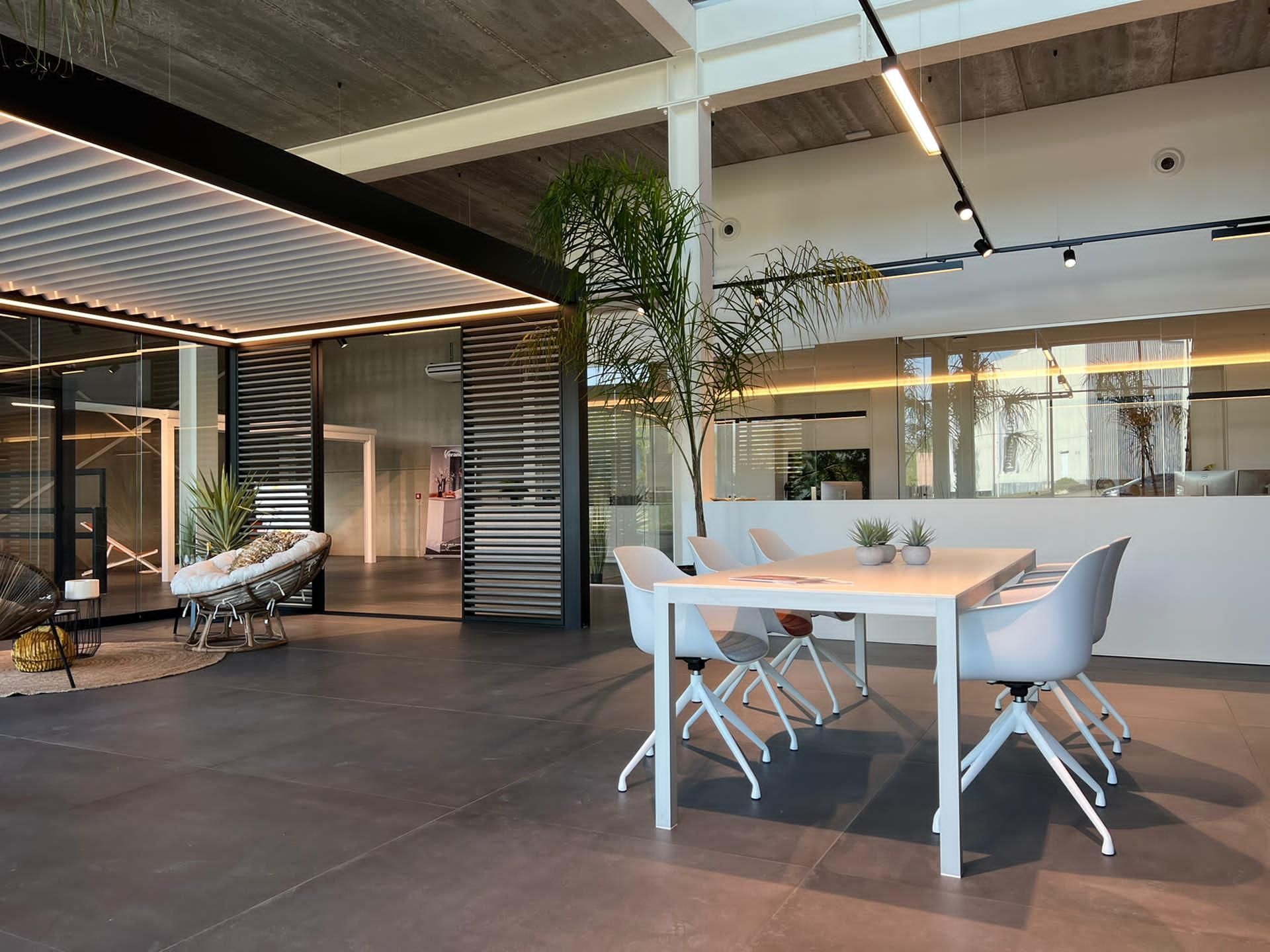 Modern kantoorinterieur met een tafel, stoelen, een zithoek en grote ramen.