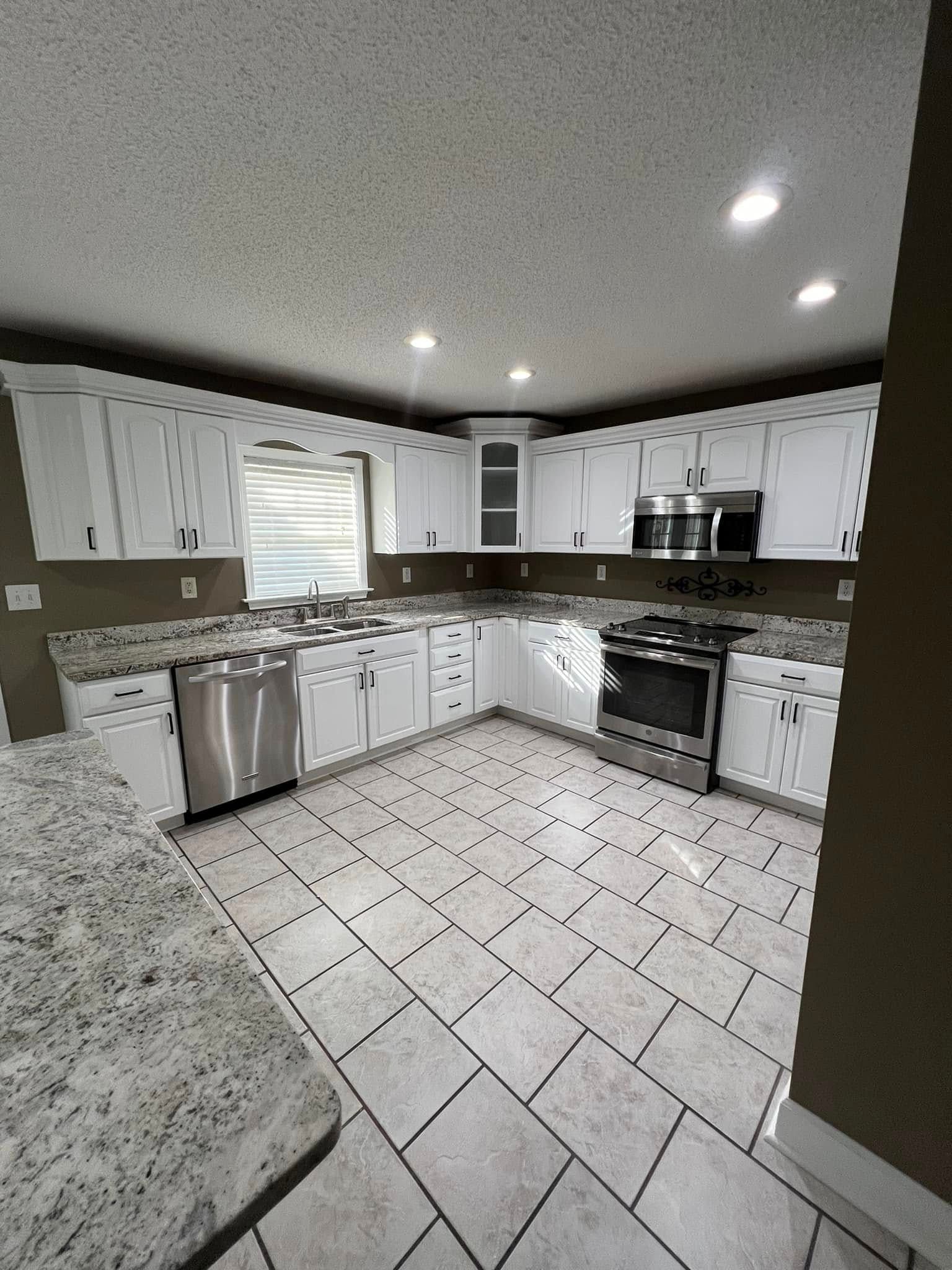 A brightly lit kitchen with white cabinets, granite countertops, stainless steel appliances, and tiled flooring.