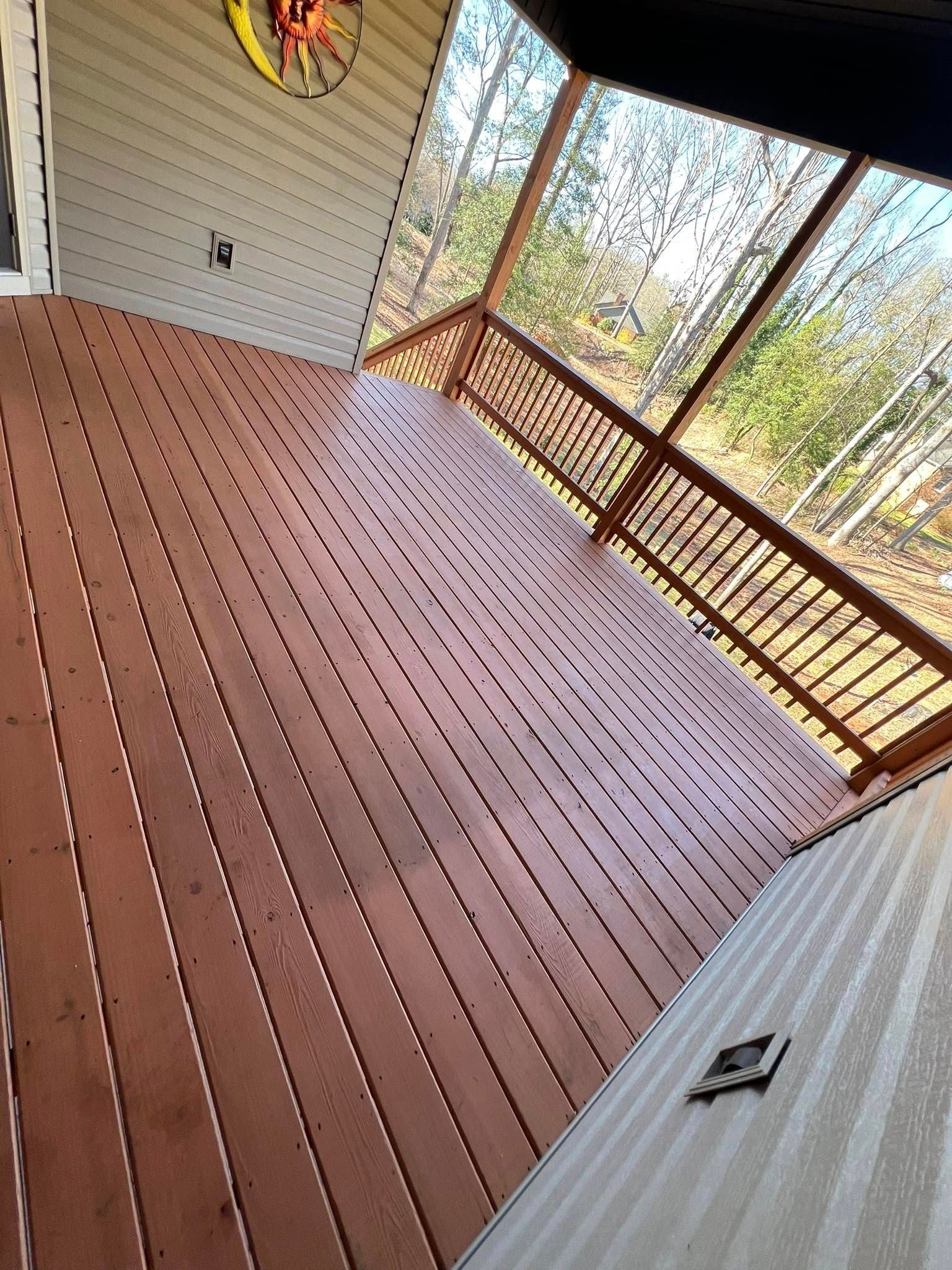 A view of a reddish-brown wooden deck on a screened-in porch, overlooking a wooded area through latticed railings.