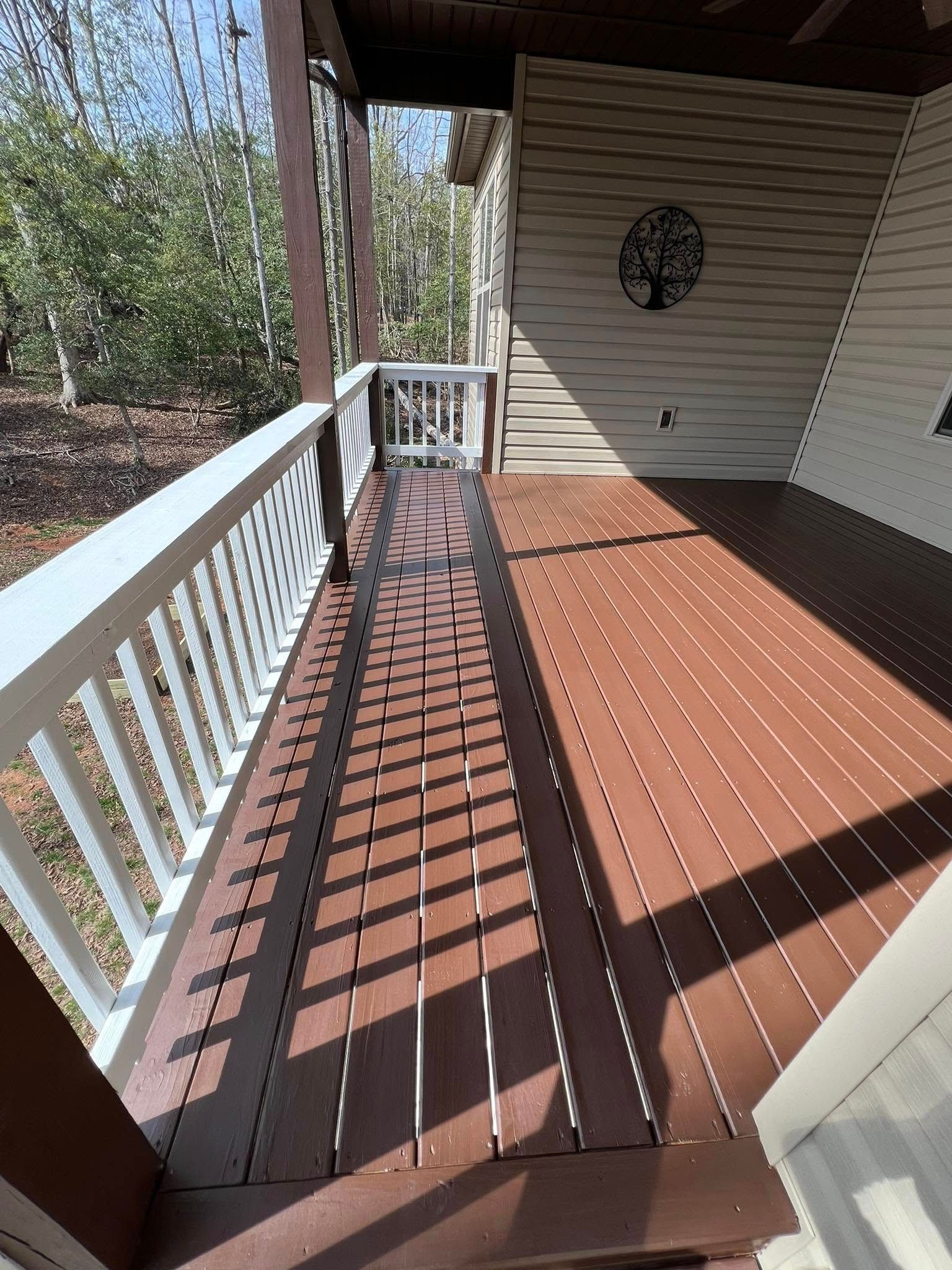 A brown wooden deck with white railing, showing a shadow pattern cast by an overhead structure.