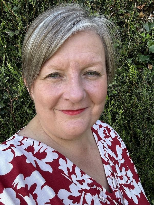 Woman in a red and white floral top smiling in front of a green hedge