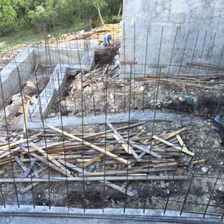 A pile of wood is laying on the ground in front of a concrete wall.
