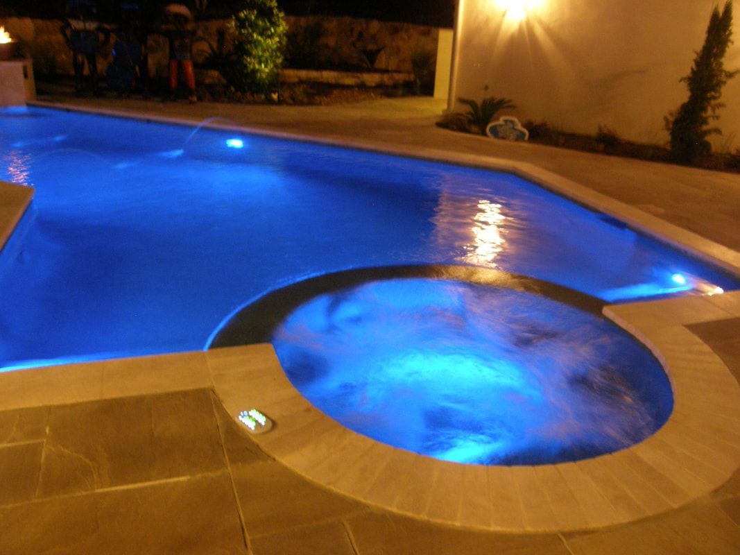 A large swimming pool is lit up at night with blue lights