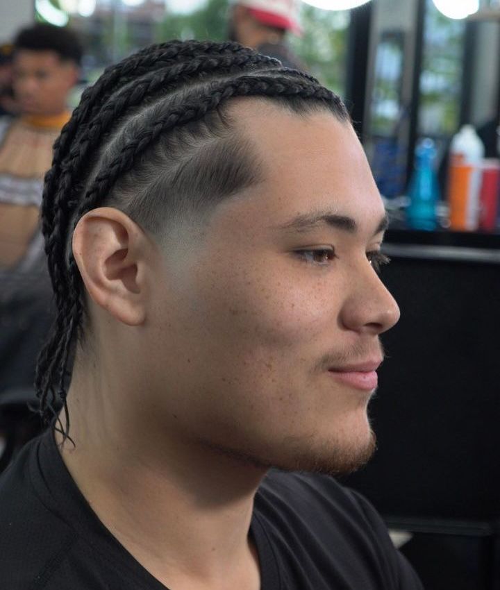 Side-profile of a person with braided hair and a short beard, smiling in a barbershop chair.