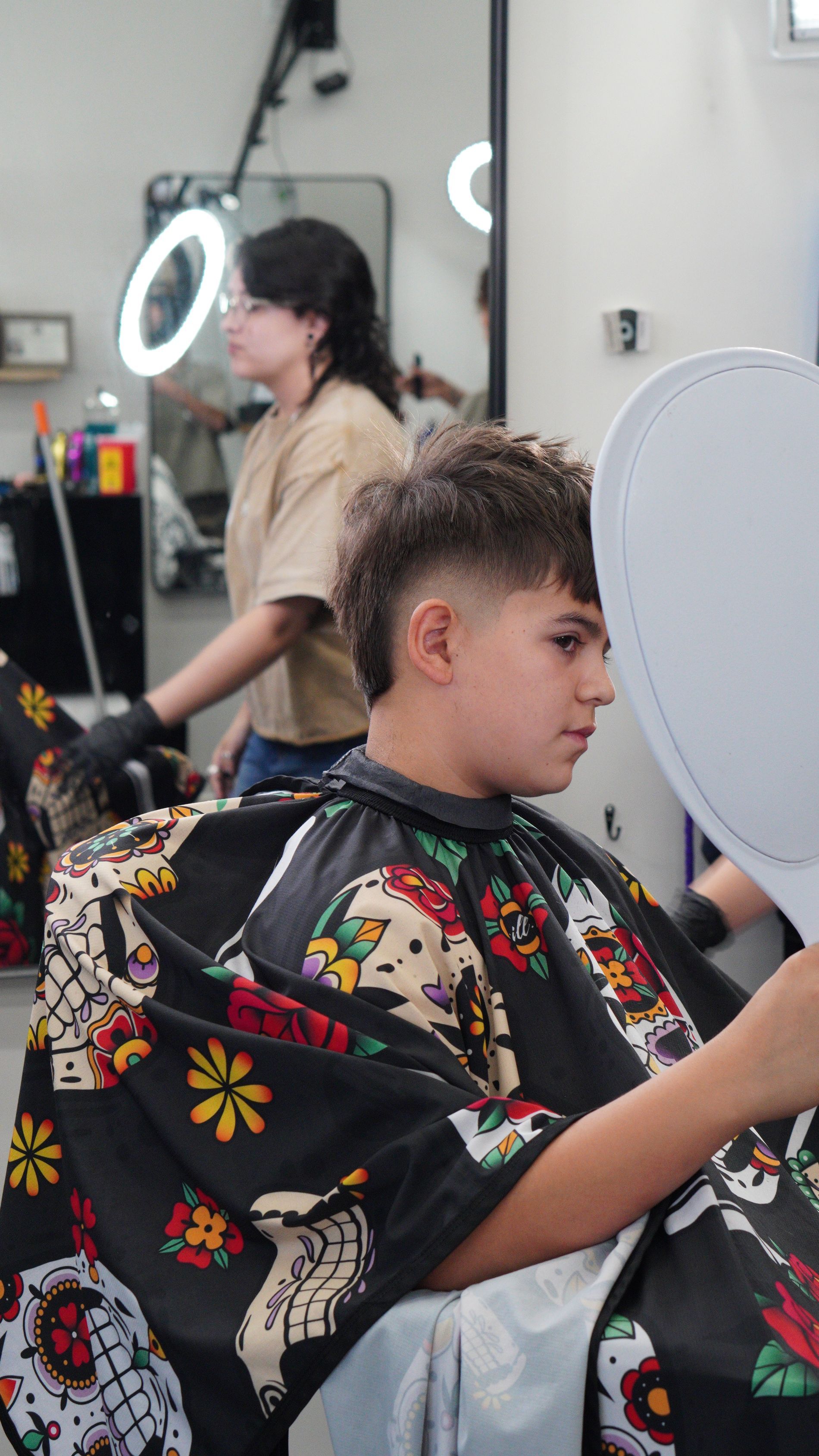 Person getting a haircut in a salon, wearing a colorful cape, with a stylist in the background.