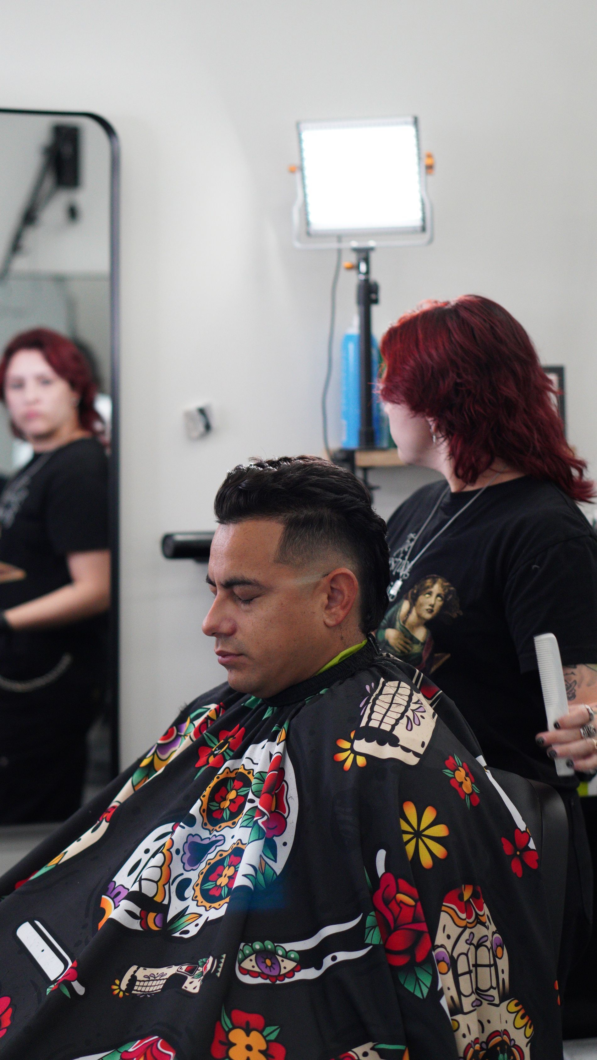 Hair salon scene with a client getting a colorful haircut while a stylist stands beside him under bright lighting