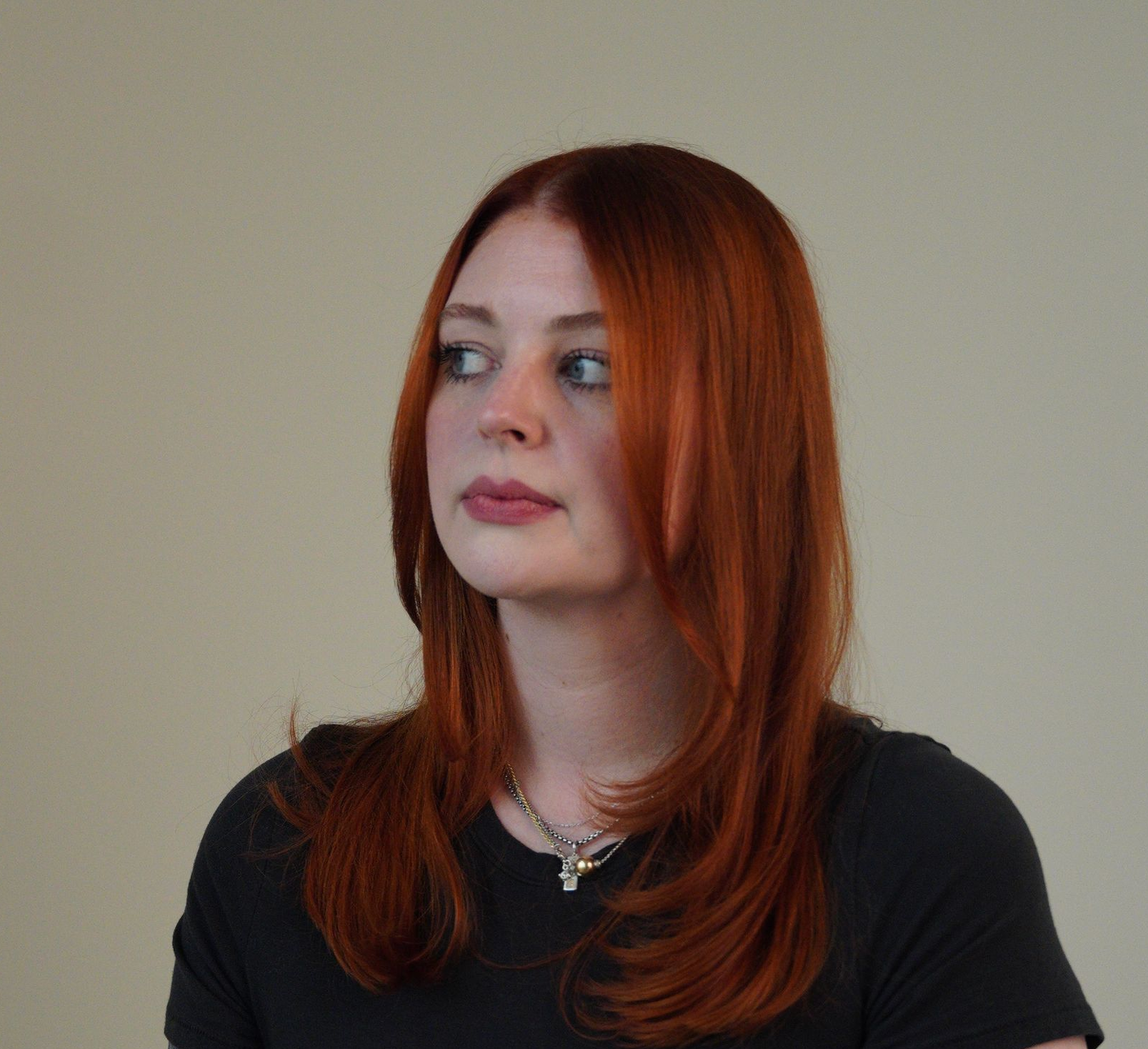 Woman with red hair in a black shirt, looking to the side against a plain beige background