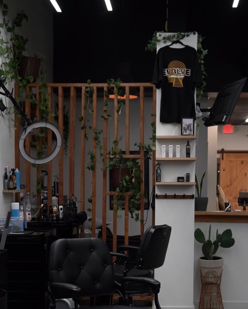 Stylish barbershop interior with black chairs, wood accents, plants, and hanging T-shirt decor