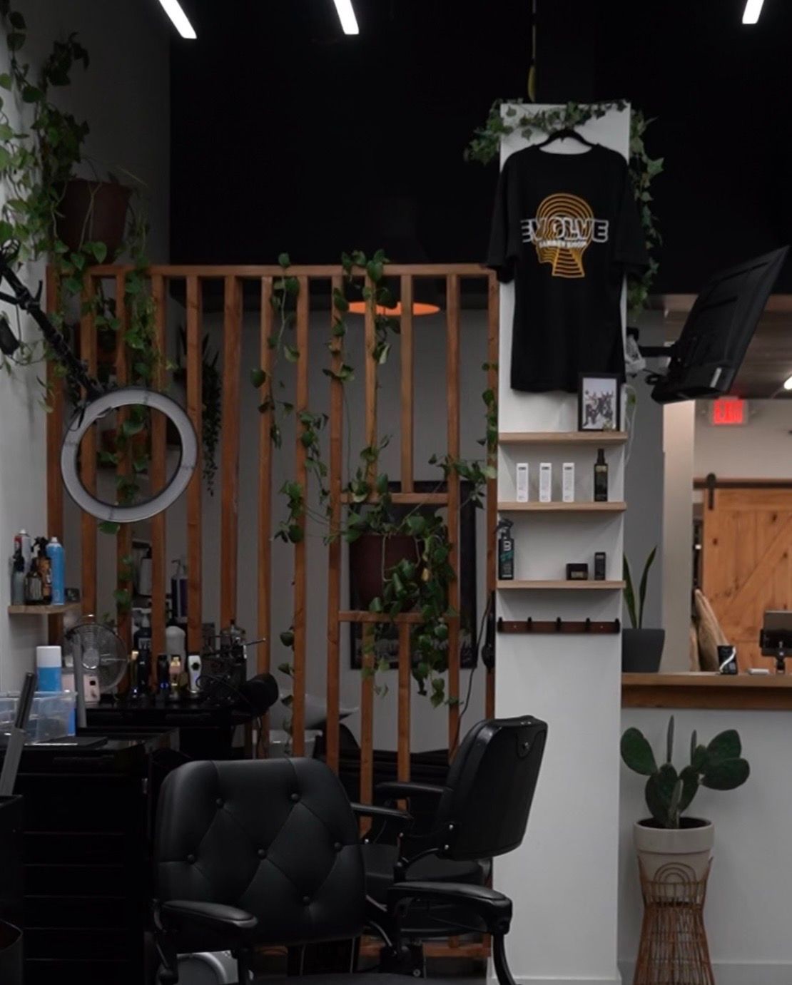 Stylish barbershop interior with black chairs, wood accents, plants, and hanging T-shirt decor