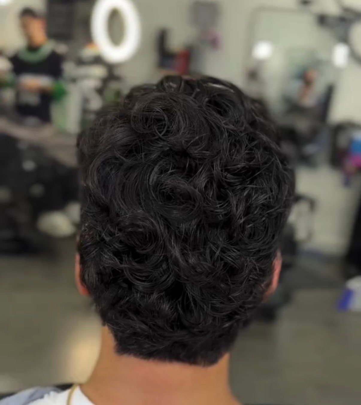 Back view of a person with short, curly dark hair in a barbershop mirror setting