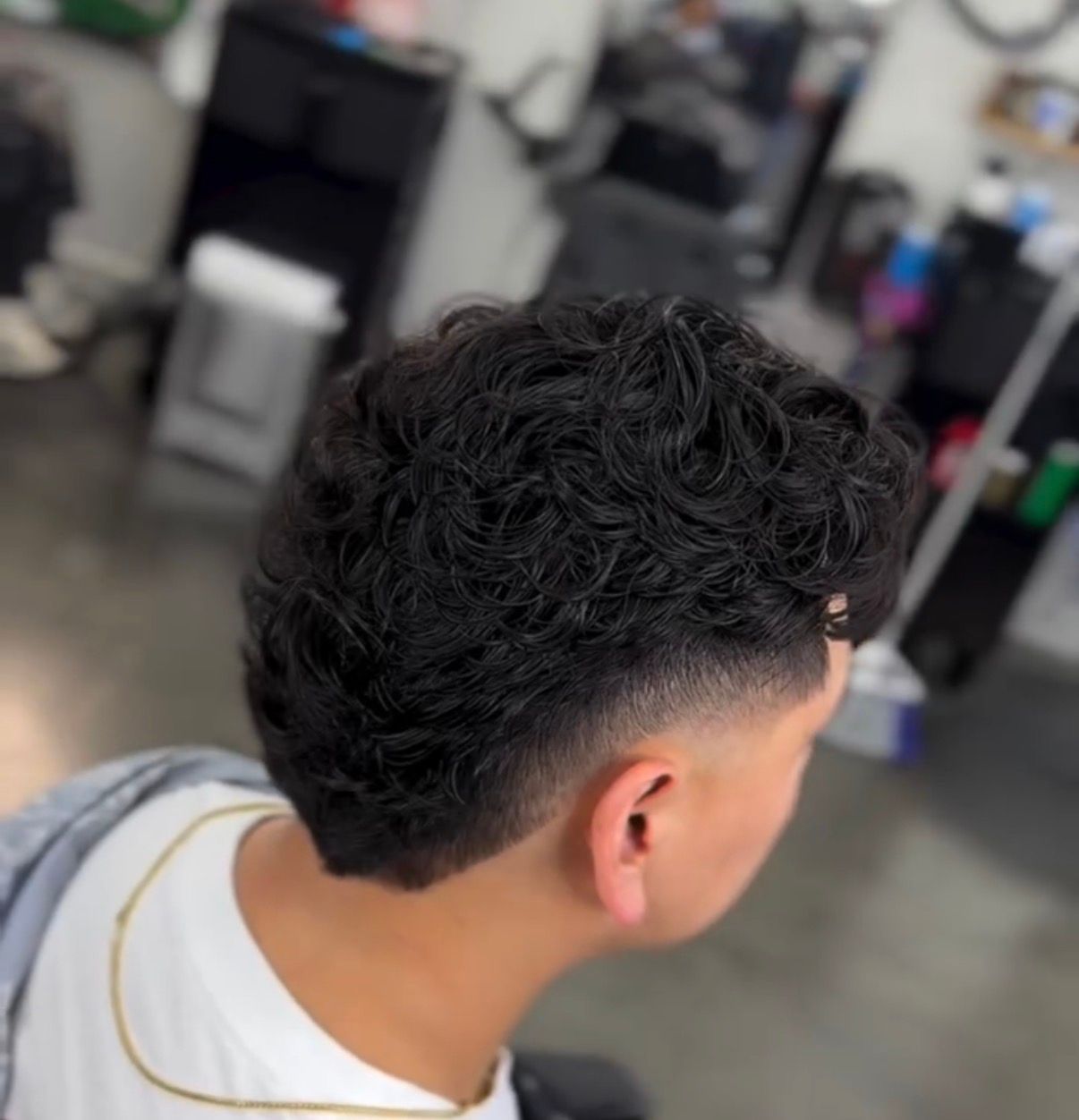 Short curly fade haircut in a barbershop, viewed from the back/side.