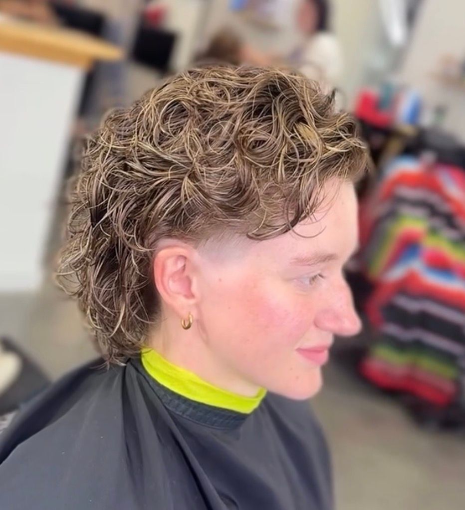 Person with short curly hair and shaved sides in a salon chair, wearing a neon green cape.