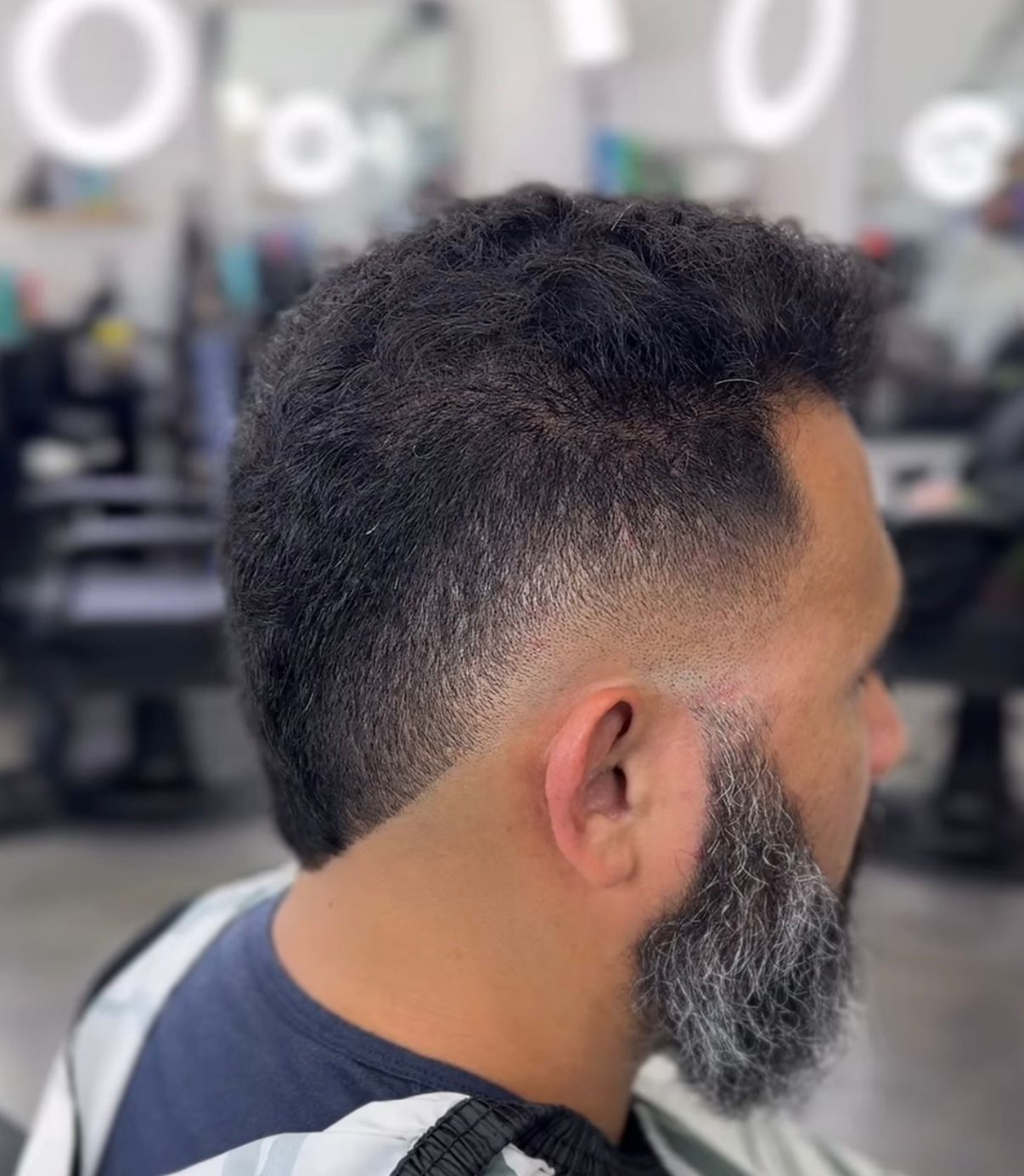 Side view of a man with a short faded haircut and gray beard in a barbershop chair