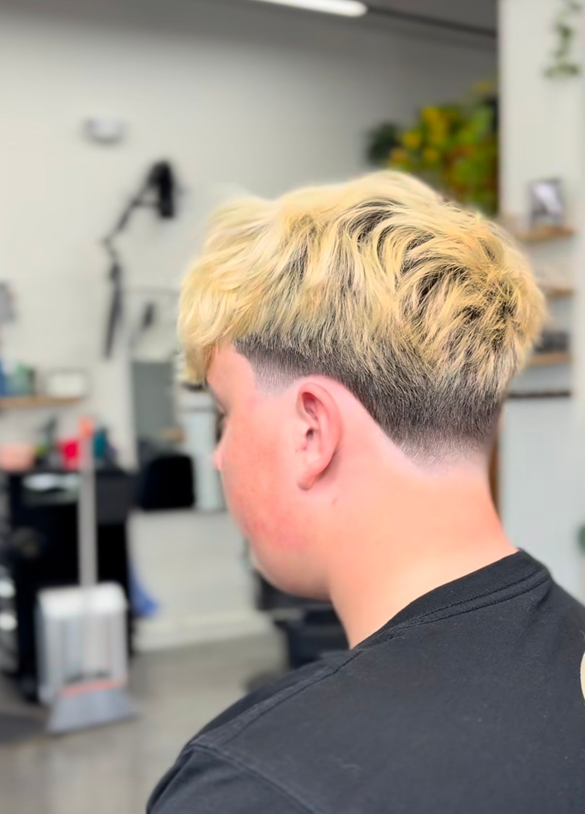 Back view of a person with blond, dark-faded hair in a barbershop chair