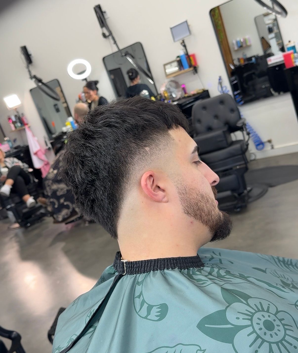 Close-up of a fresh curly fade haircut in a barbershop, with a green cape draped over the client.