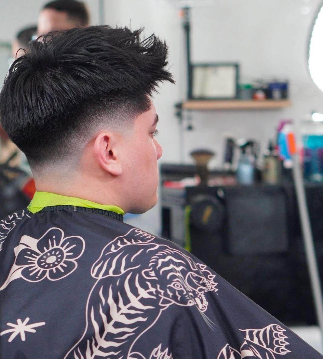 Side view of a person with a short fade haircut in a barber chair, wearing a floral cape.