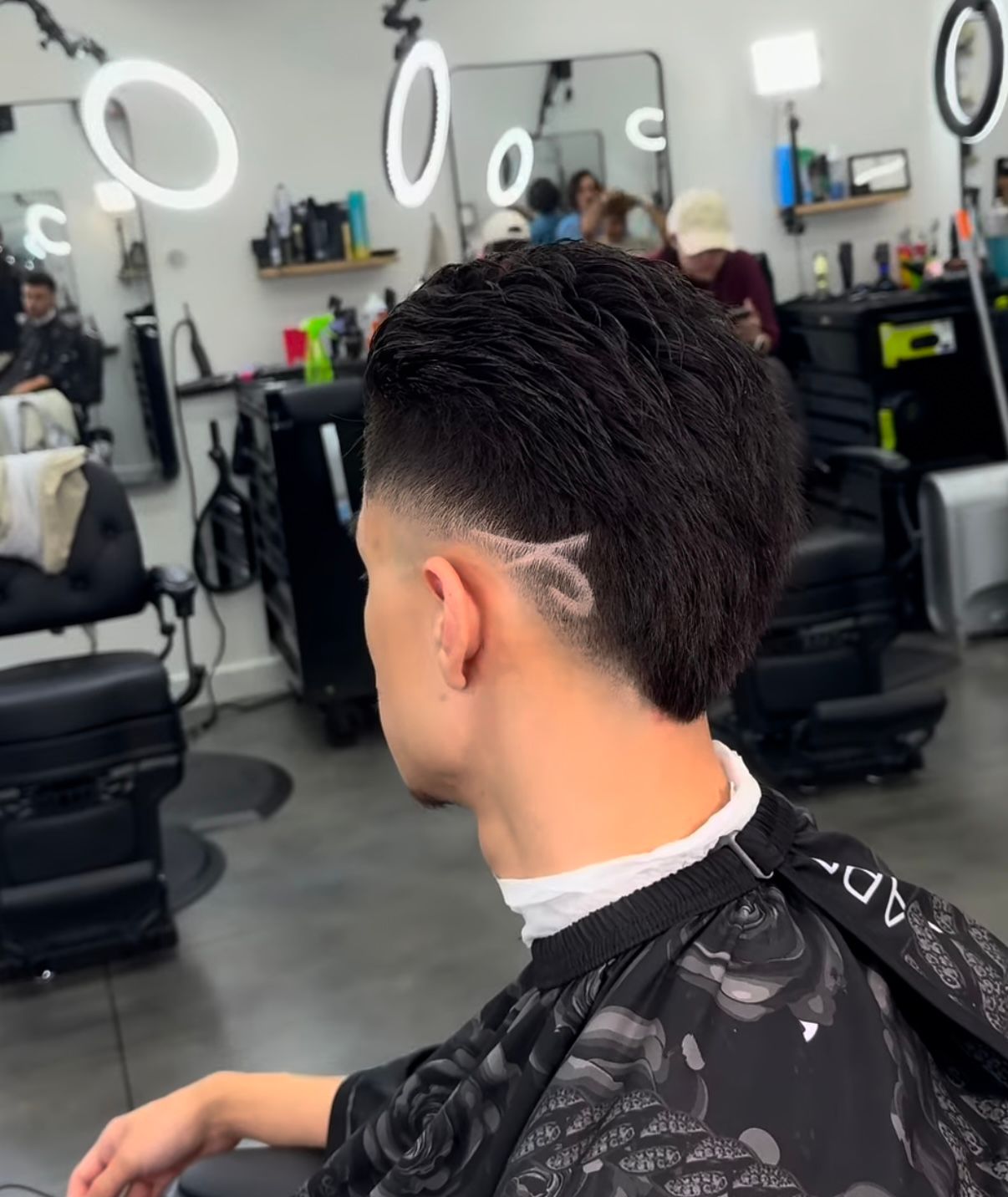 Man getting a fresh fade haircut in a modern barbershop, seen from behind.