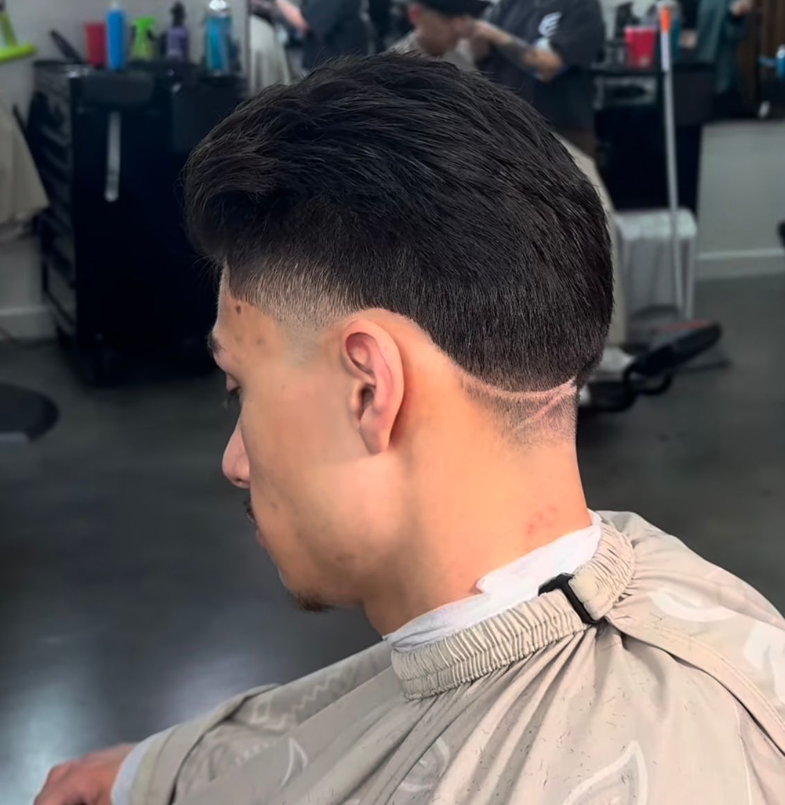 Man with a low fade haircut in a barber chair, side view, wearing a beige cape
