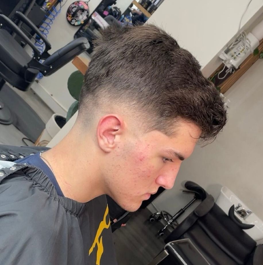 Young person in a barber chair with a fresh fade haircut, looking down in a barbershop.