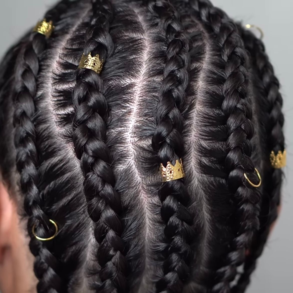 Close-up of braided black hair with gold beads and rings on a gray background