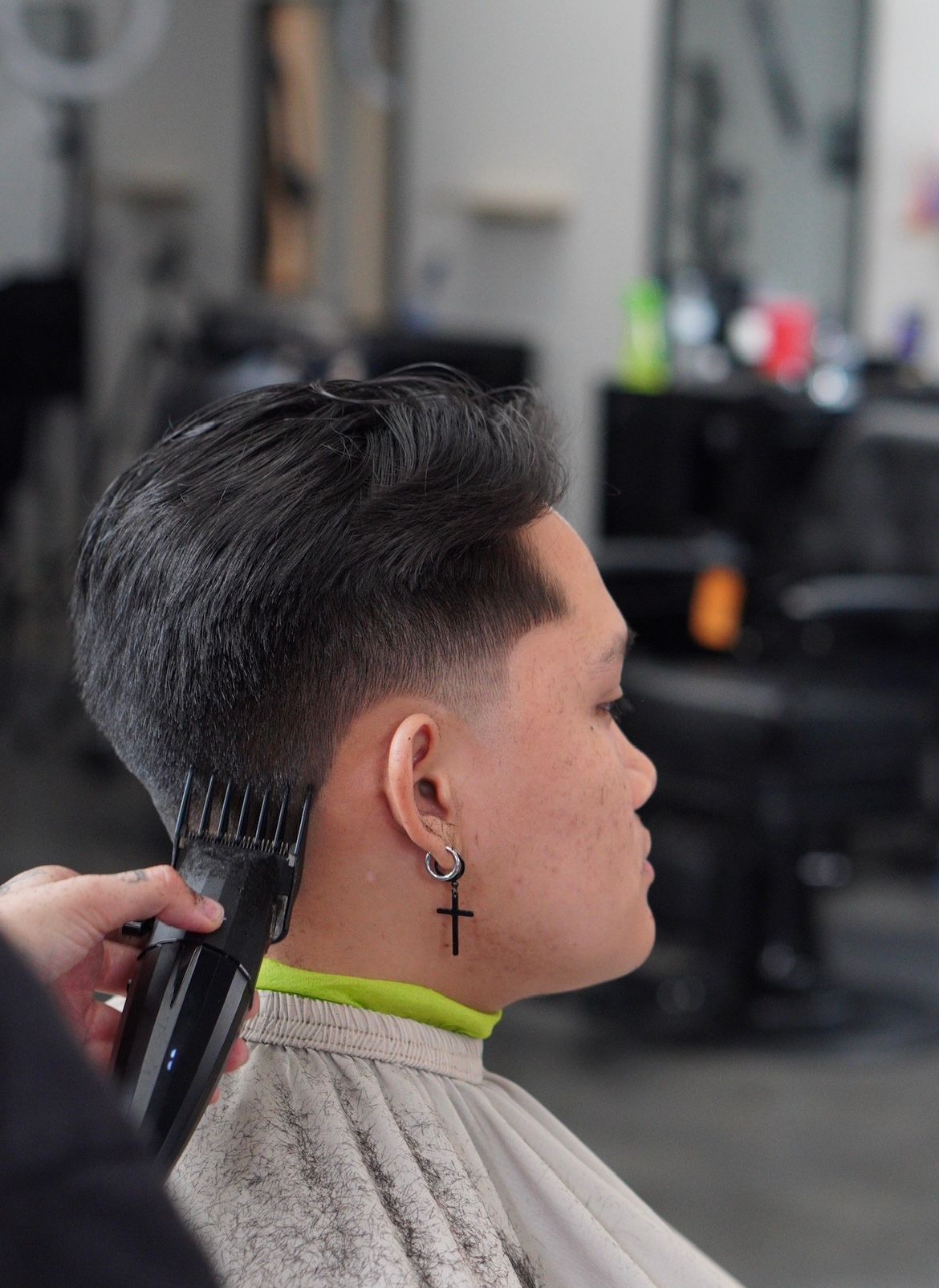 Side profile of a person with a short fade haircut getting a trim in a barbershop.