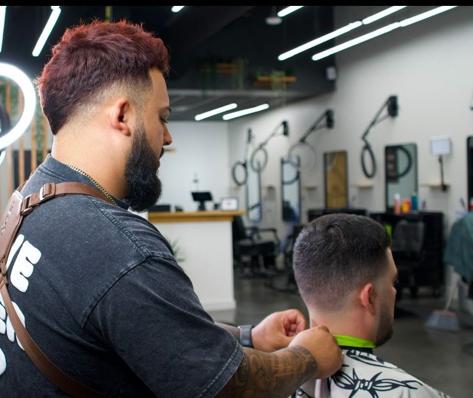 Barber trimming a man’s hair in a modern barbershop with bright overhead lights