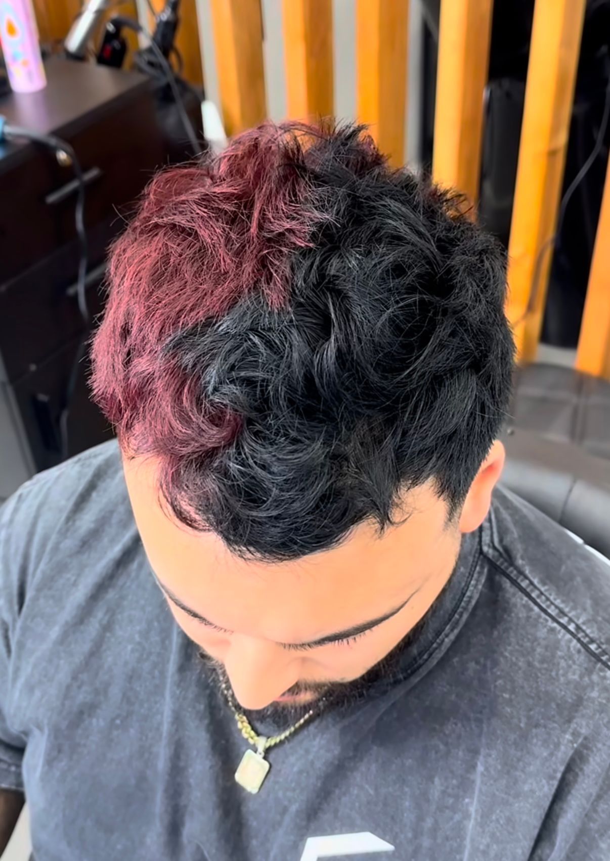 Top-down view of a person with split red and black curly hair, looking down in a salon chair