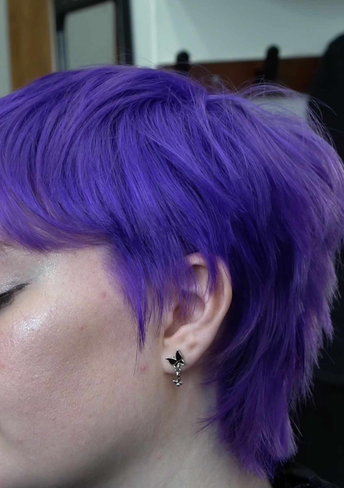 Profile view of a person with vivid purple short hair and a small black earring.