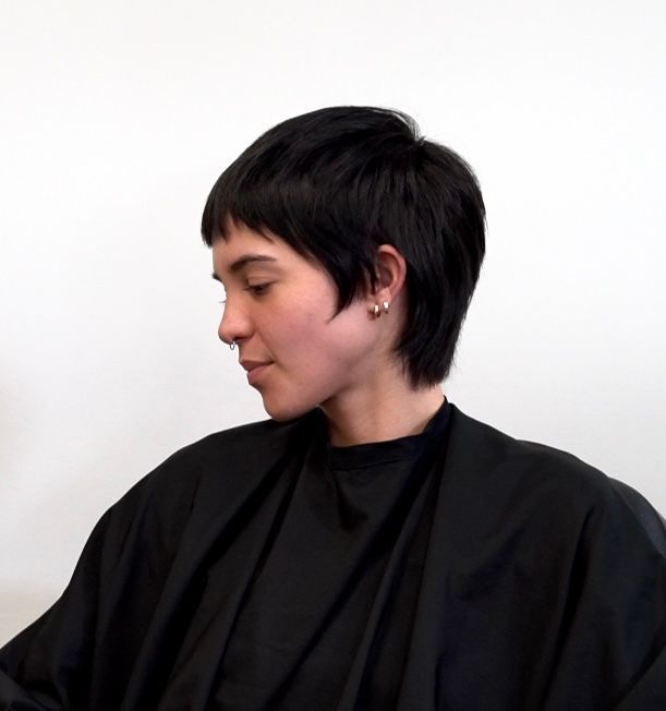 Profile of a person with short dark hair and black clothing against a plain white background