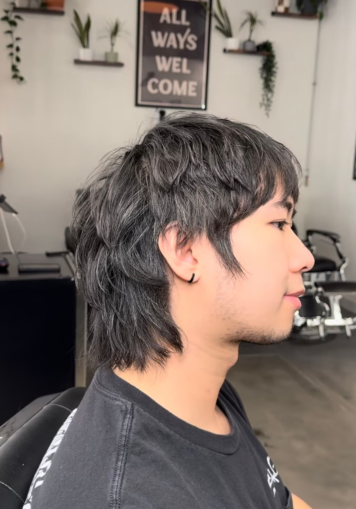Side profile of a person with short dark hair in a salon interior, wearing a black shirt.