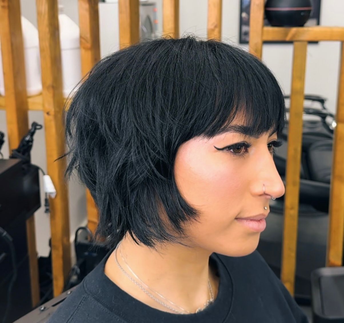 Side-profile portrait of a person with short black hair in a salon setting