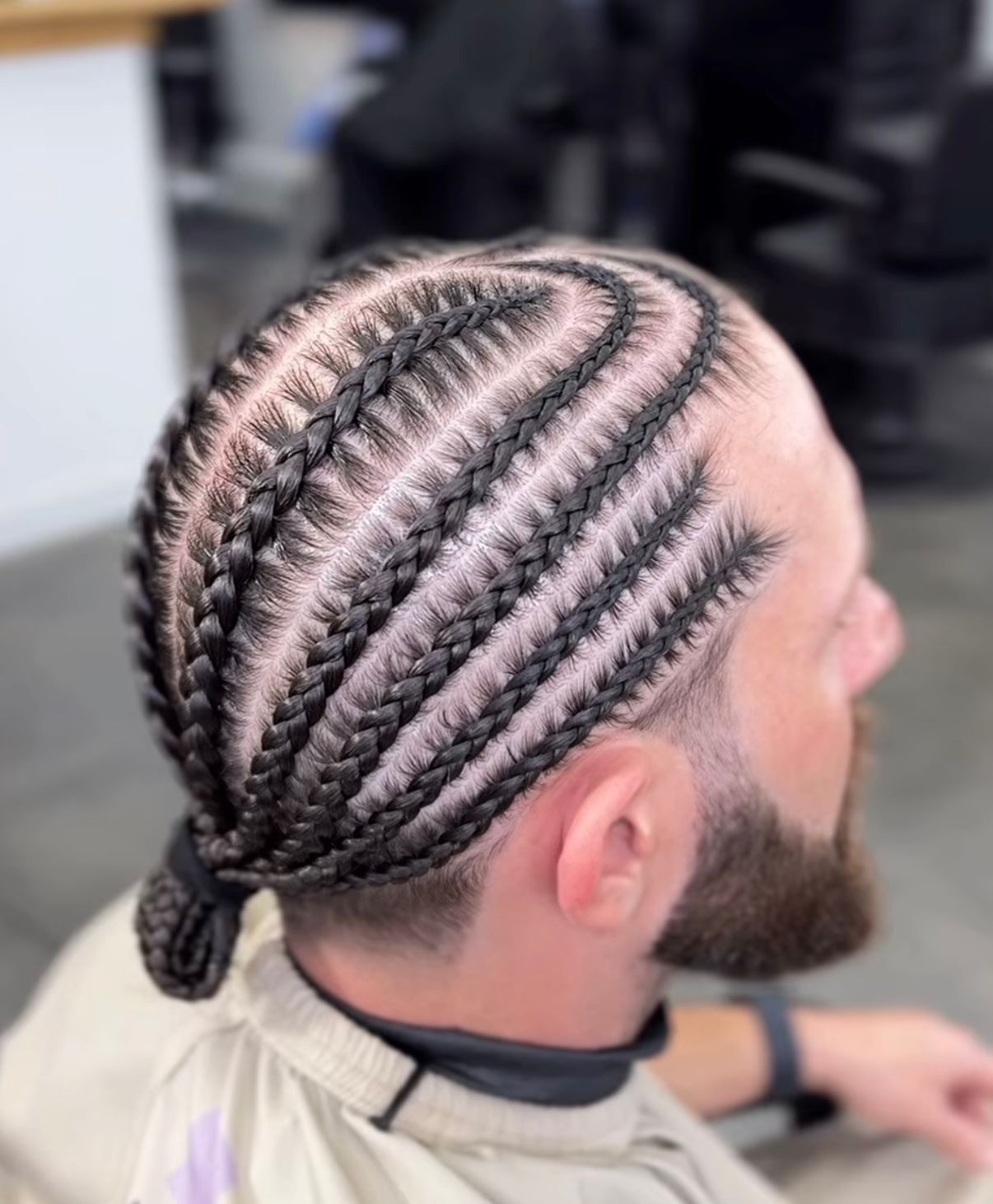 Close-up of intricate braided cornrows with a small bun on the back of a seated person’s head