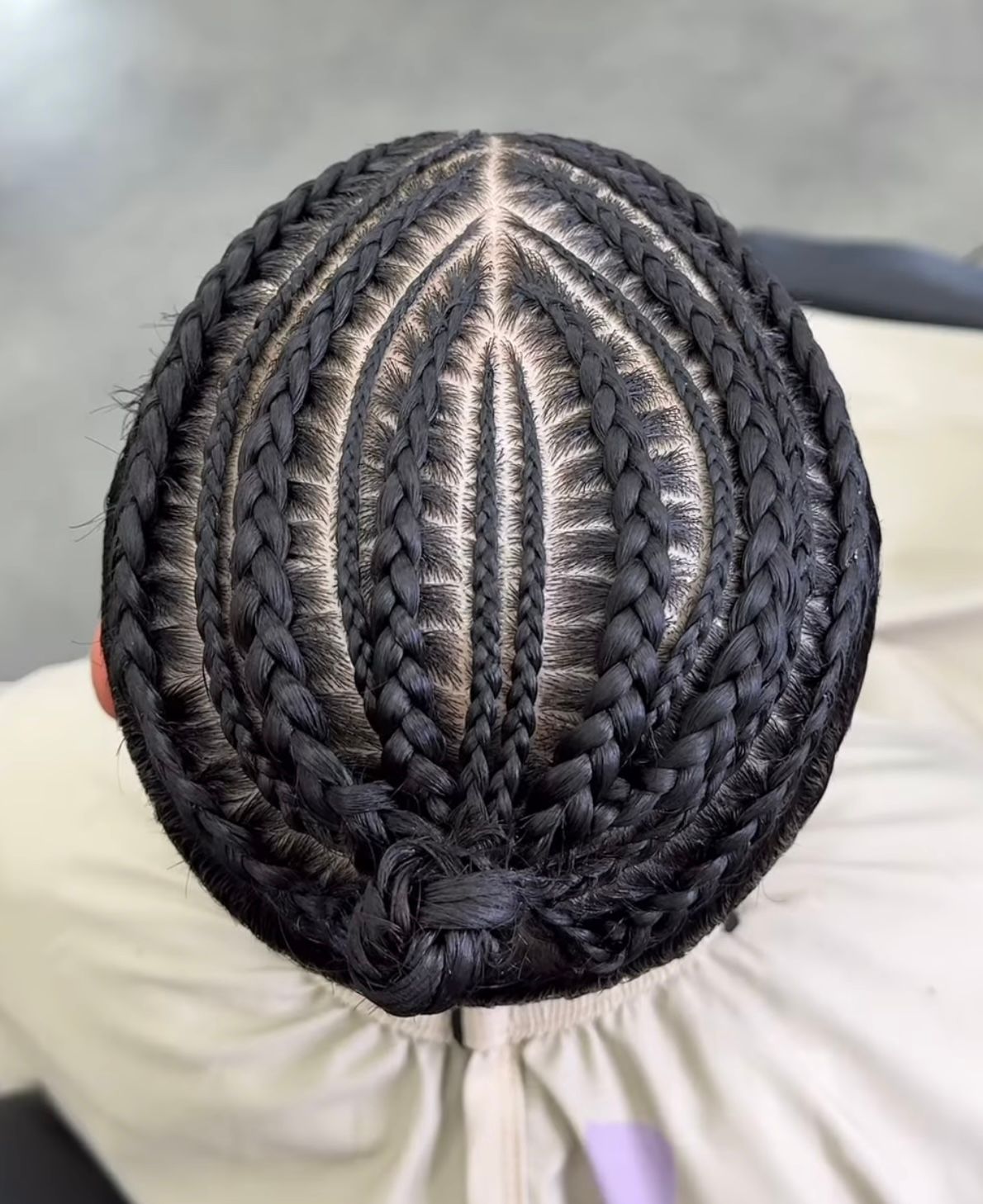 Top view of neatly braided black cornrows with a center part on a light background