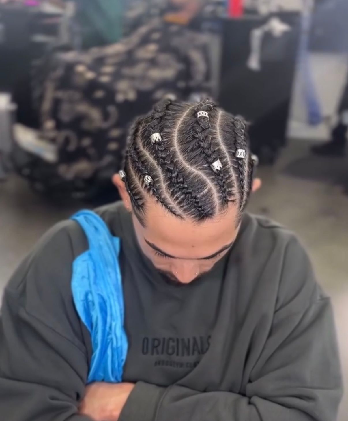 Person with braided cornrows looking down, wearing a dark sweatshirt with a blue towel over one shoulder.