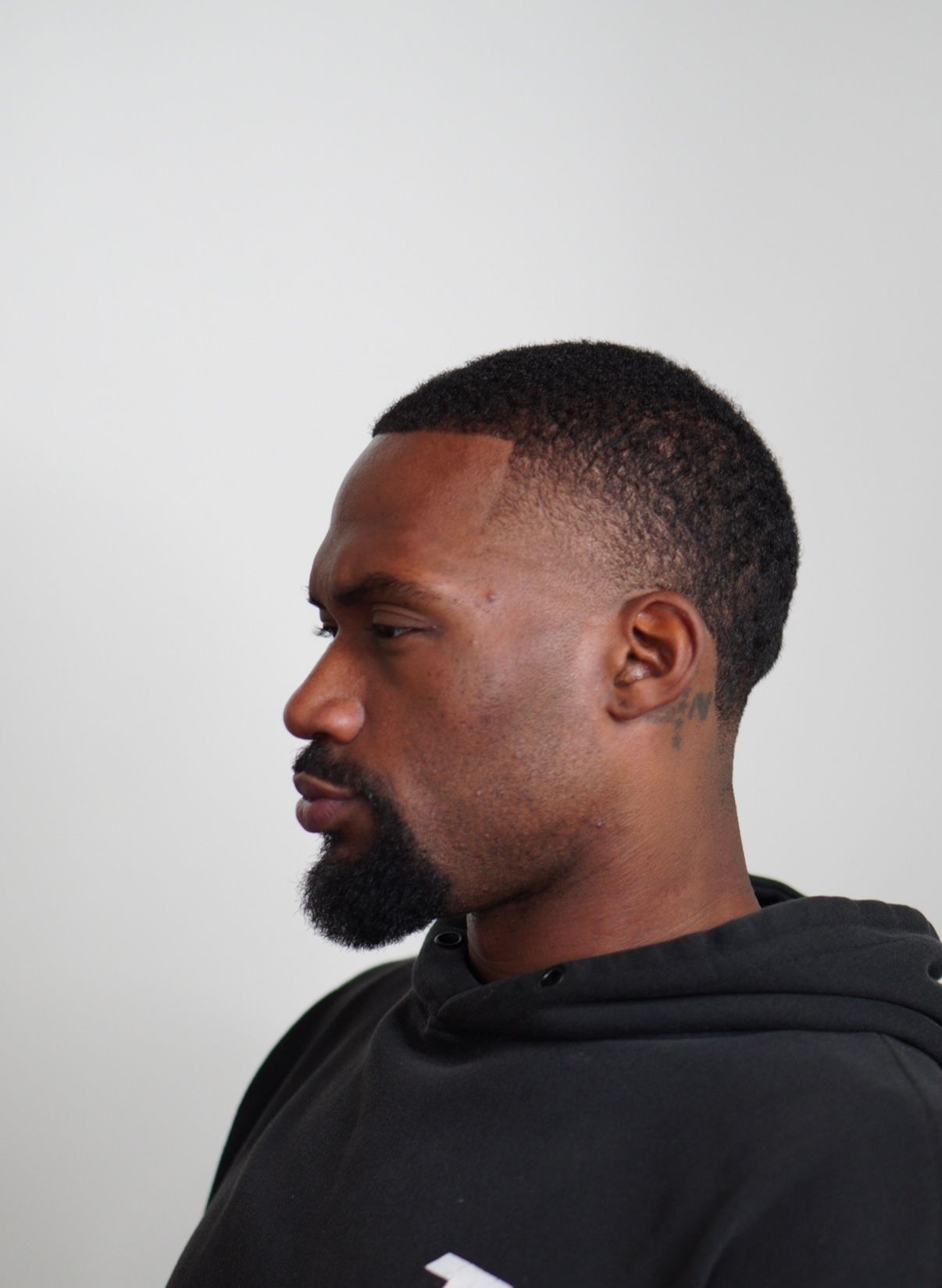 Side profile of a man in a black hoodie against a light gray background.
