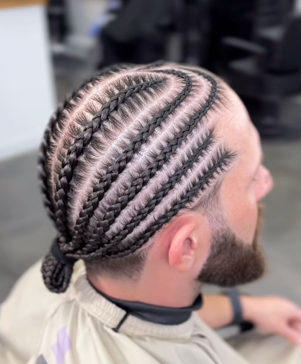 Man with cornrow braids and a beard, viewed from above in a barber chair