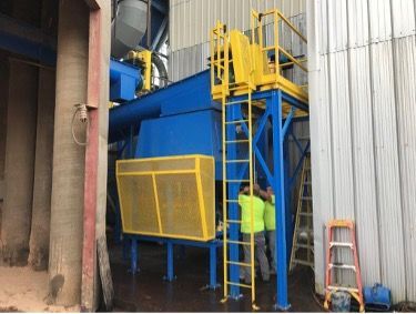 Blue industrial machine with yellow accents; two workers, one climbing a ladder.