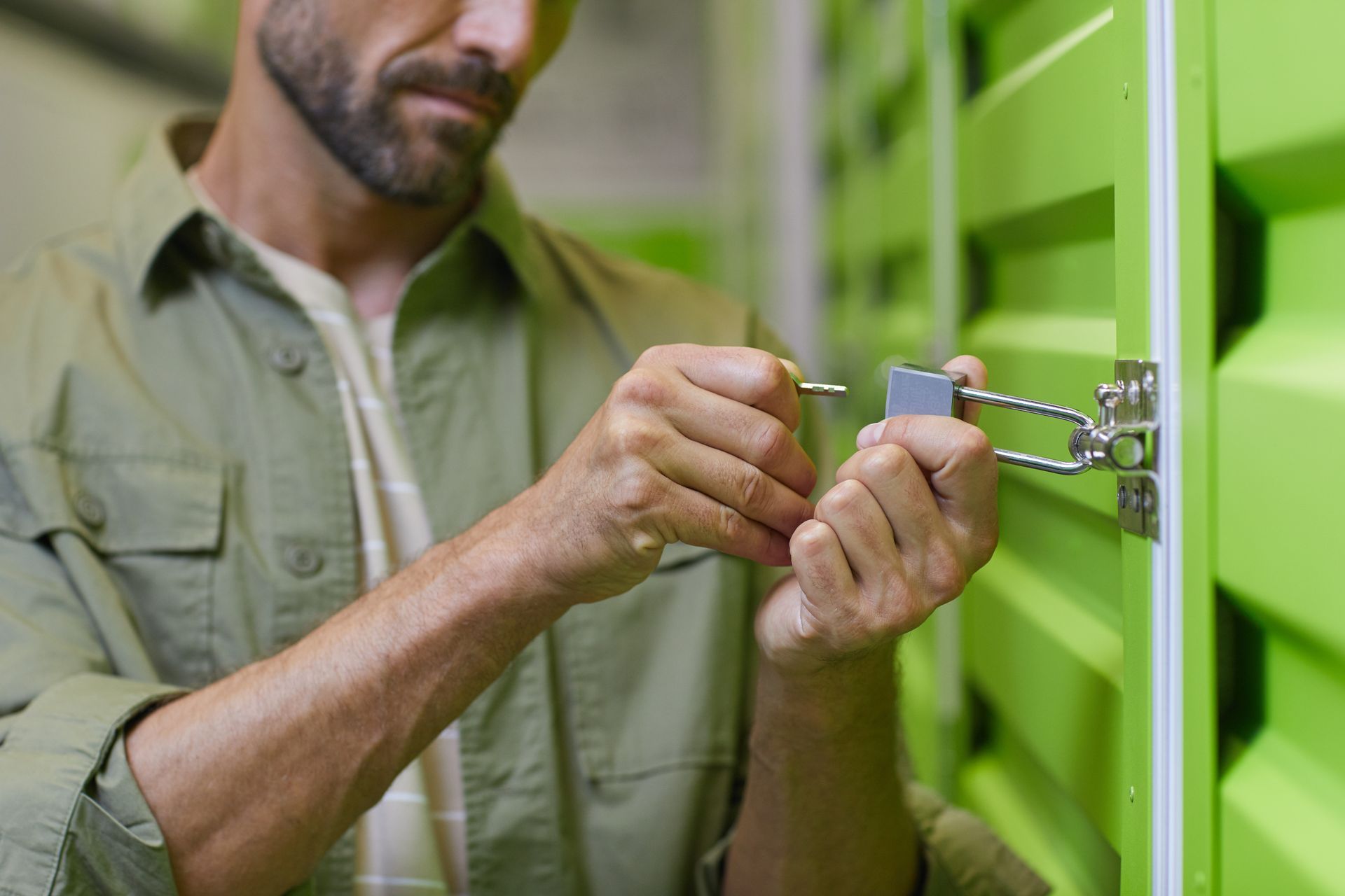 A close-up of a man opening a padlock on the door of a self-storage unit.
