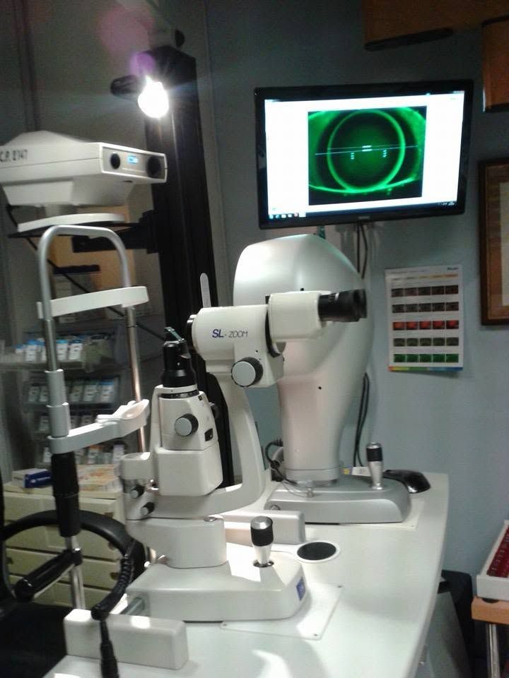 Sala per visite optometriche con apparecchiature per esami della vista e uno scanner retinico verde su un monitor